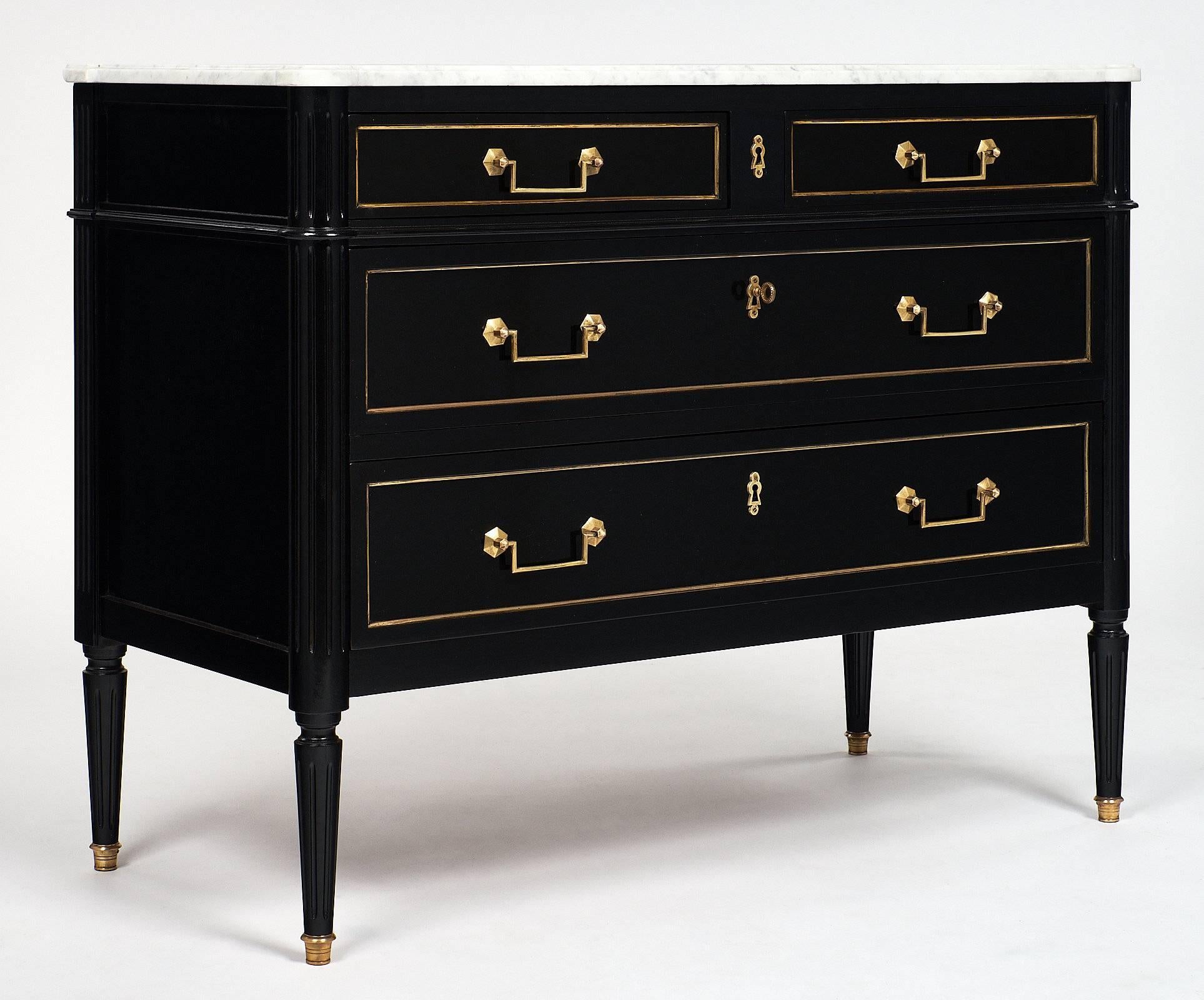 French Louis XVI chest of drawers of mahogany, ebonized and finished with a lustrous French polish. It also has a Carrara marble top and tapered legs capped with brass feet. There are four dovetailed drawers enhanced with gilt brass trims and finely