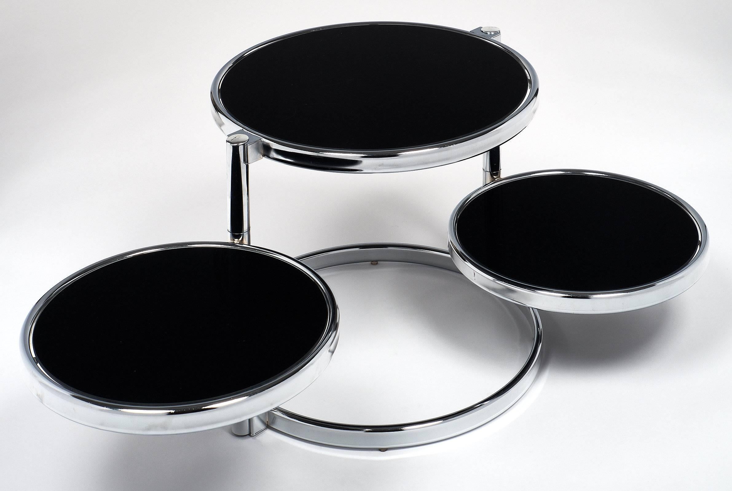 Polished chrome and black glass modern side table. This piece has a circular top, with two shelves that can be turned below the top or pulled out for use. Each surface has black glass for a modernist, elegant look. The shelves each have a diameter