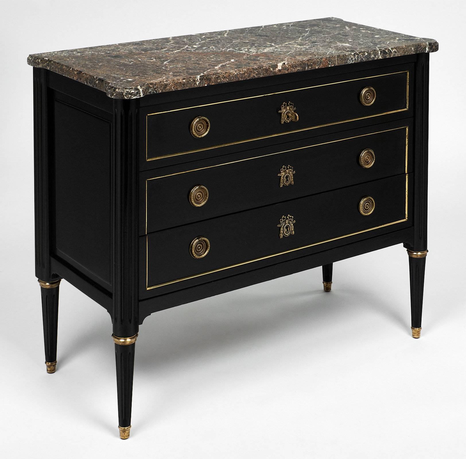 Classic Louis XVI style chest of drawers made of mahogany and featuring a striking Sainte Anne marble slab top. This piece has been ebonized and finished with a lustrous French polish. The drawers are trimmed with brass, and the tapered legs are