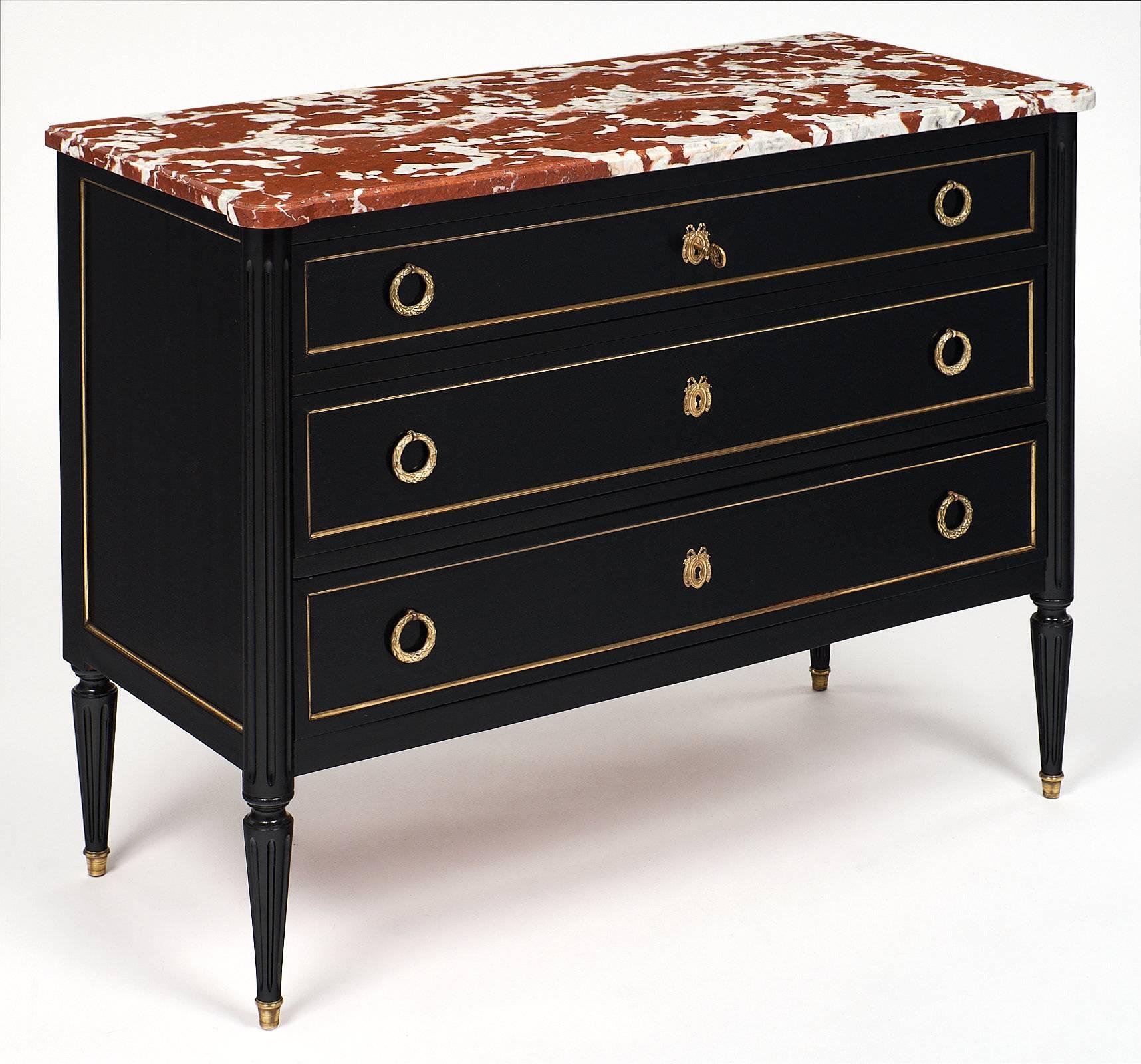 This French antique Louis XVI style chest boasts a unique red marble “rouge royal” top with striking white veining. The trim on both sides and around all three drawers, the stylized pull handles, and the ribbon escutcheons with working keys are all