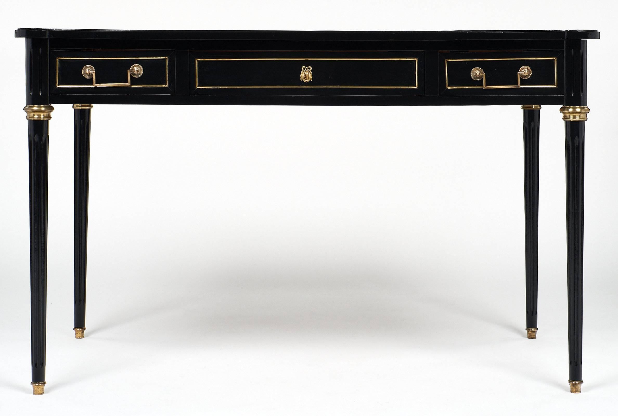 French antique Louis XVI style desk with brown-gray leather top and original brass trim, hardware, and decor. The mahogany wood is ebonized and finished with a lustrous French polish. This piece has two small drawers on either side of one large