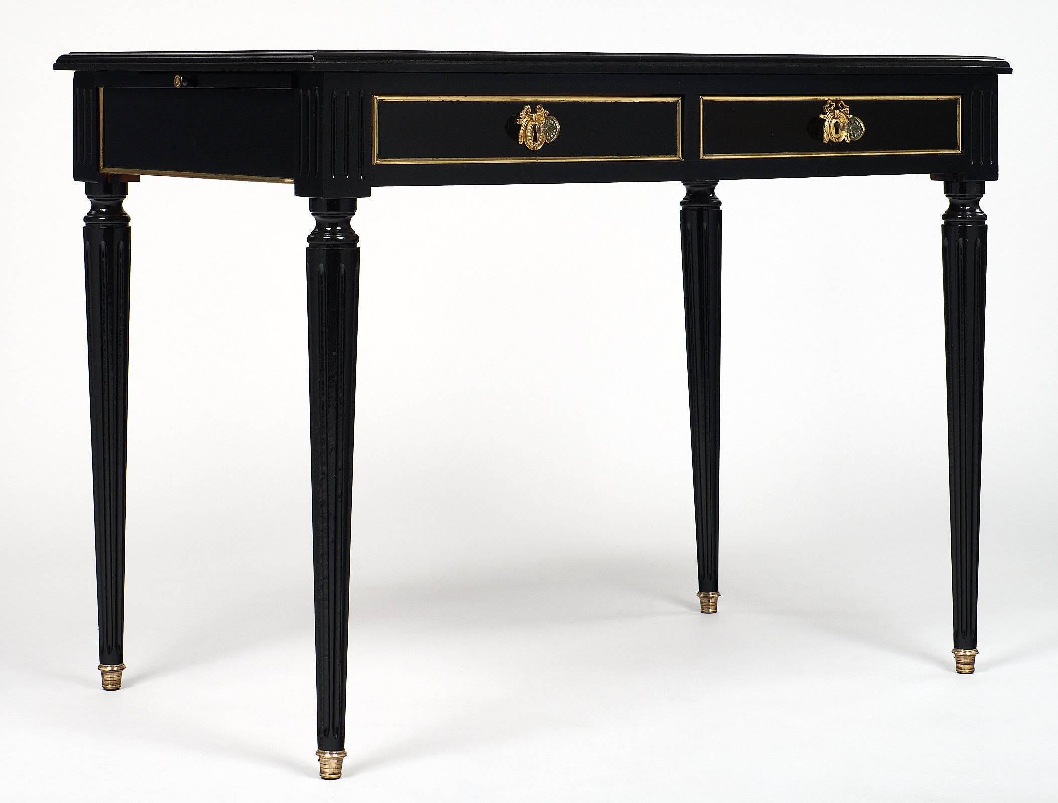 Ebonized Louis XVI style writing desk, with original cognac leather top with 23 carat gold-embossed frieze detail. The front of the piece has two drawers with brass trim, stylized brass escutcheons, and working keys. The other three sides also have