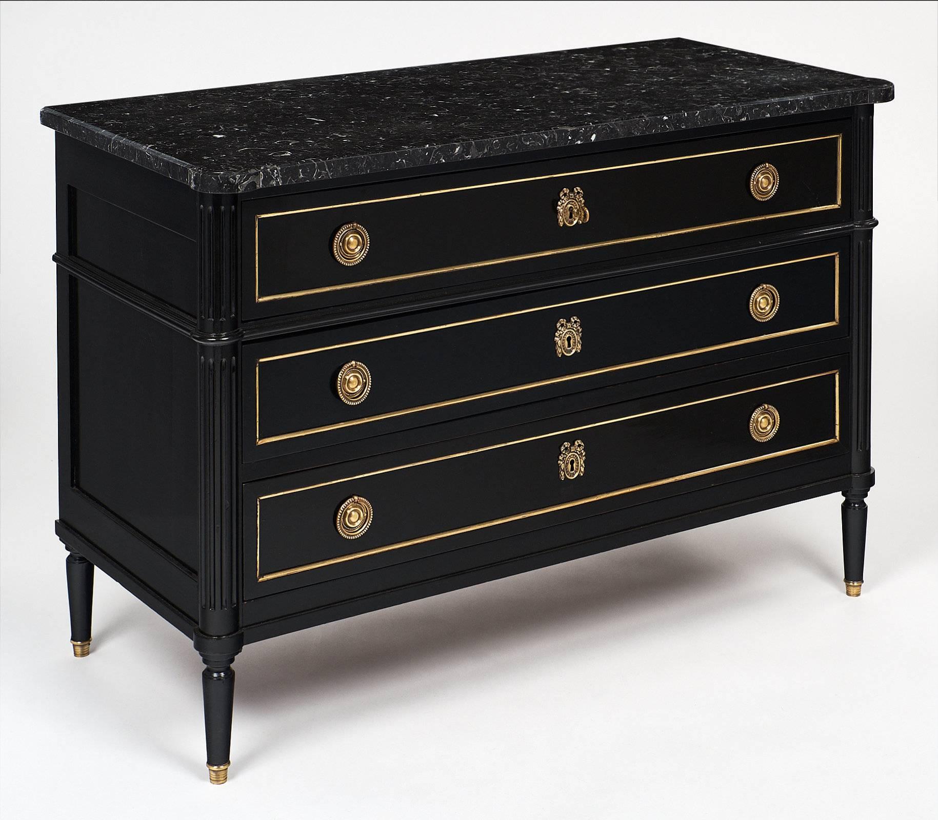 Antique French Louis XVI style chest with an ebonized, lustrous French polish finish and black marble top. The brass trim, capped feet and stylized brass handles and escutcheons are all original. The hand-carved fluted corners, dovetail drawers,