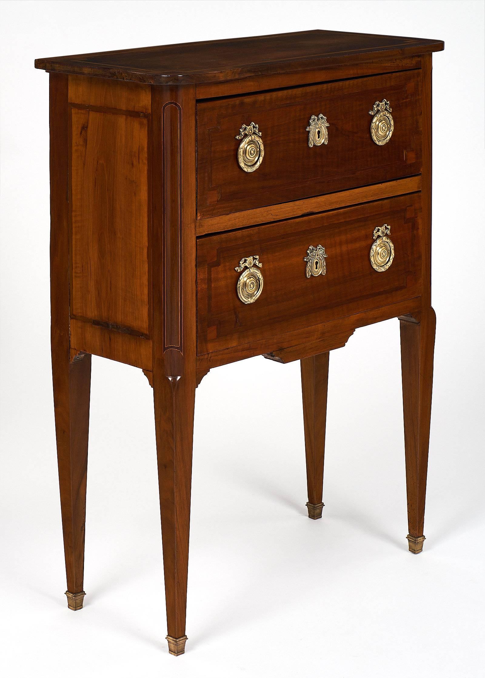 This perfectly proportioned Louis XVI style piece is made from mahogany, with hand-crafted inlays on each drawer, sides, and top. The finely cast brass hardware and escutcheons are all original. The long, tapered legs are each capped with brass as