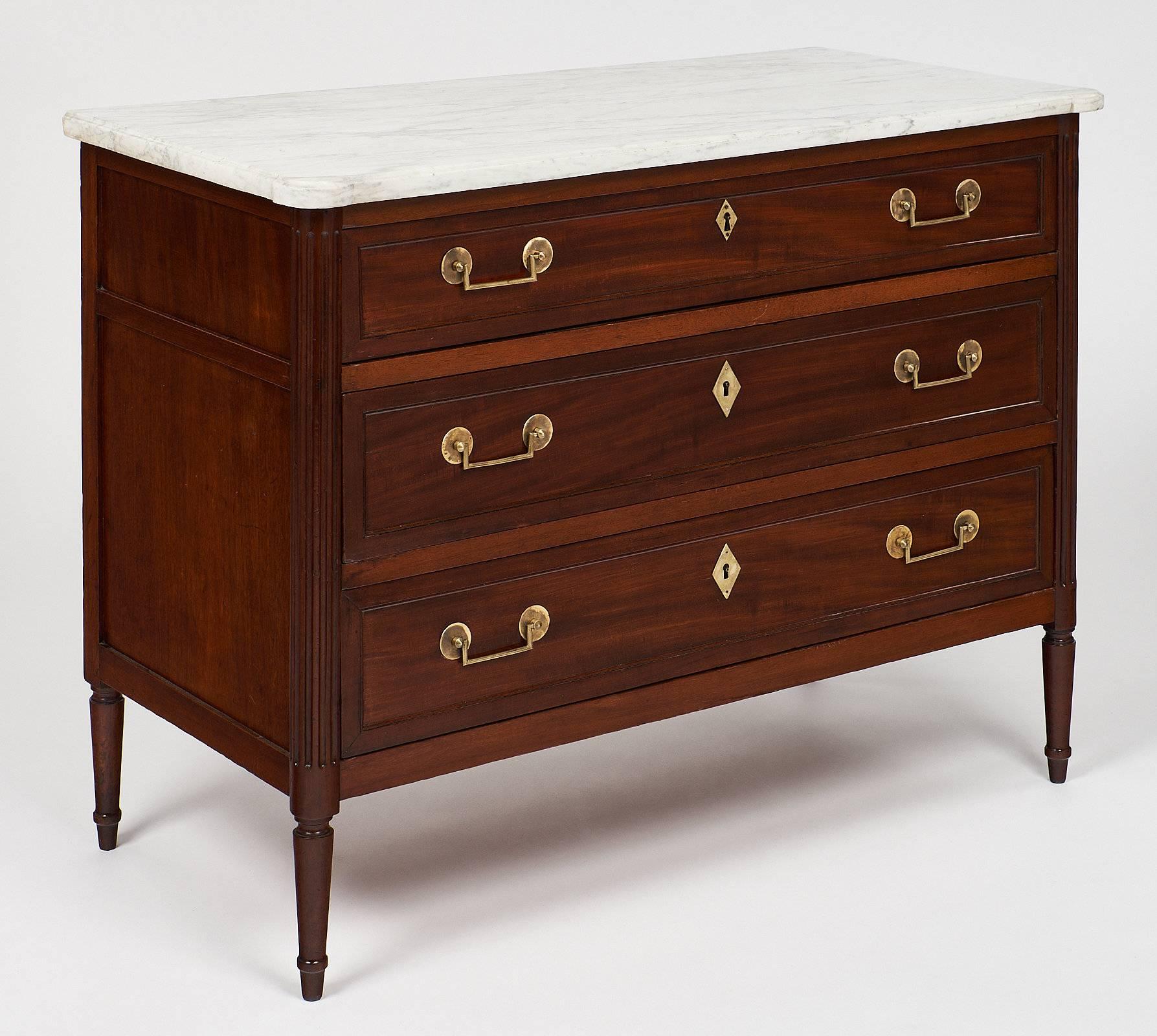 A fine French mahogany chest of three dovetailed drawers. Oak was used as a secondary wood, and gilt brass trim is found throughout. It has tapered “toupie” legs. The “commode” features an original and very clean Carrara marble slab, lightly veined.