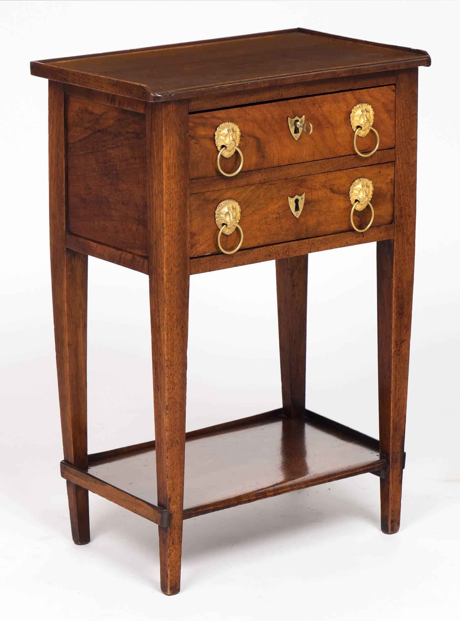 French Consulat period side table in solid burl walnut and solid elm, with original ormolu lion head hardware, finely cast, on two dovetailed drawers; tapered legs; and bottom shelf.