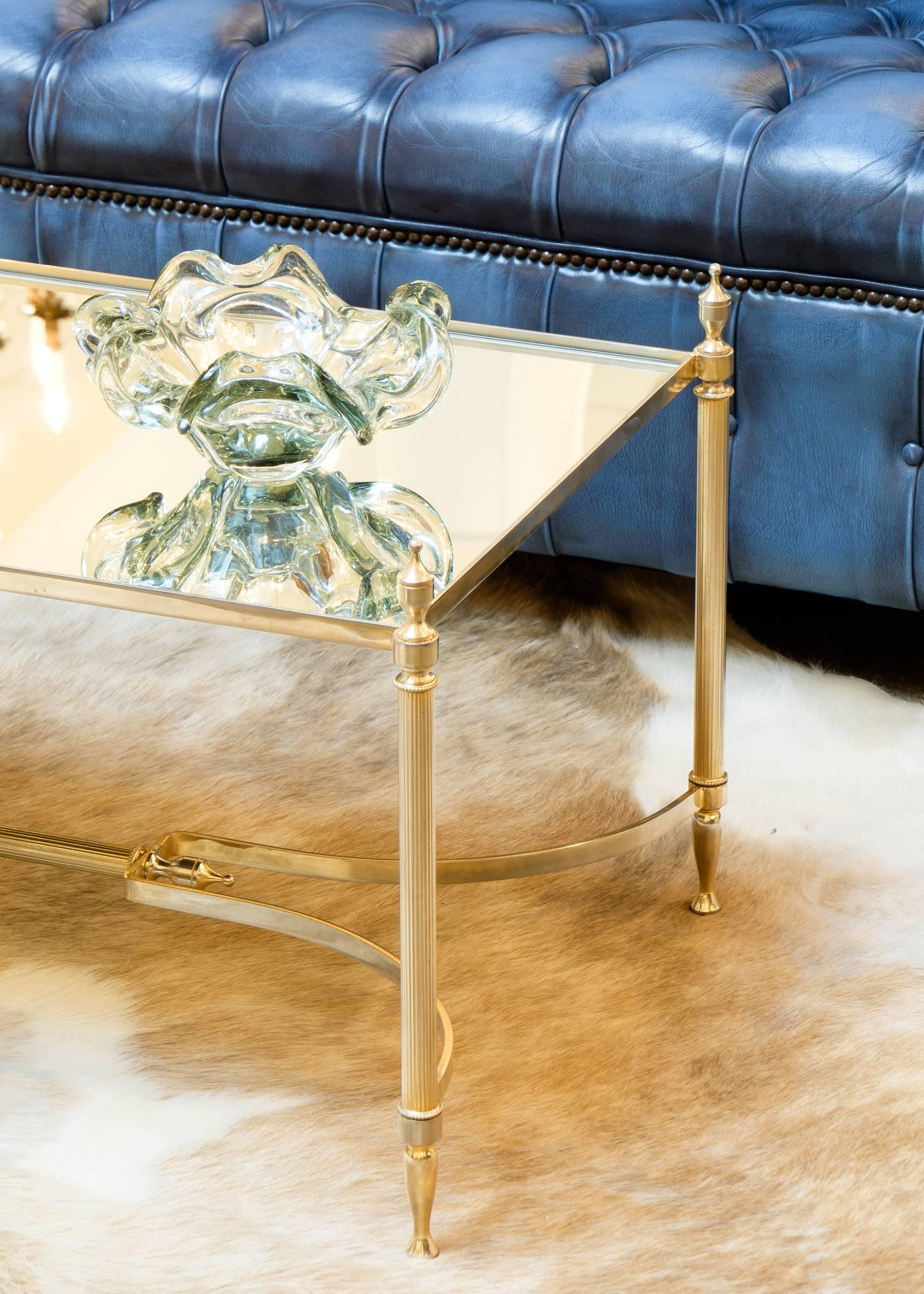 French vintage cocktail table in brass with a mirrored glass top. We adore the neoclassic flair with stylized finials, fluted legs, and arched stretcher. A refined and elegant piece.