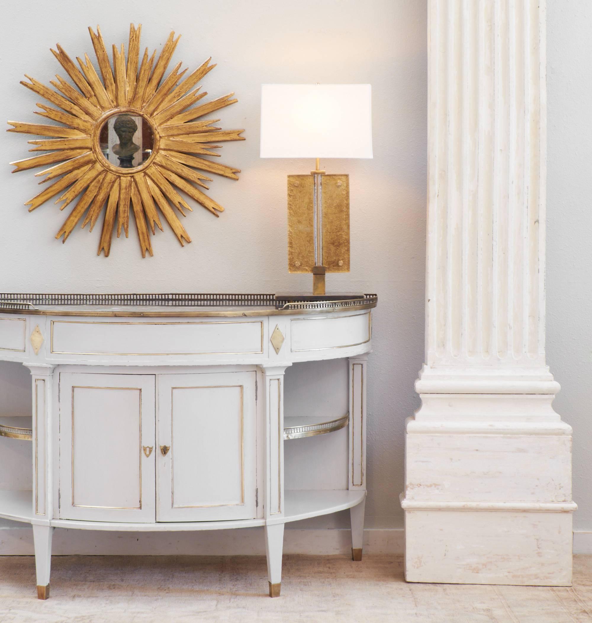 Antique French Directoire style demilune sideboard with gray Saint Anne marble top, resplendent with brass trim and galleries. Solid cherrywood with a light gray patina, open shelves and two doors, on tapered legs with brass feet. The piece was in