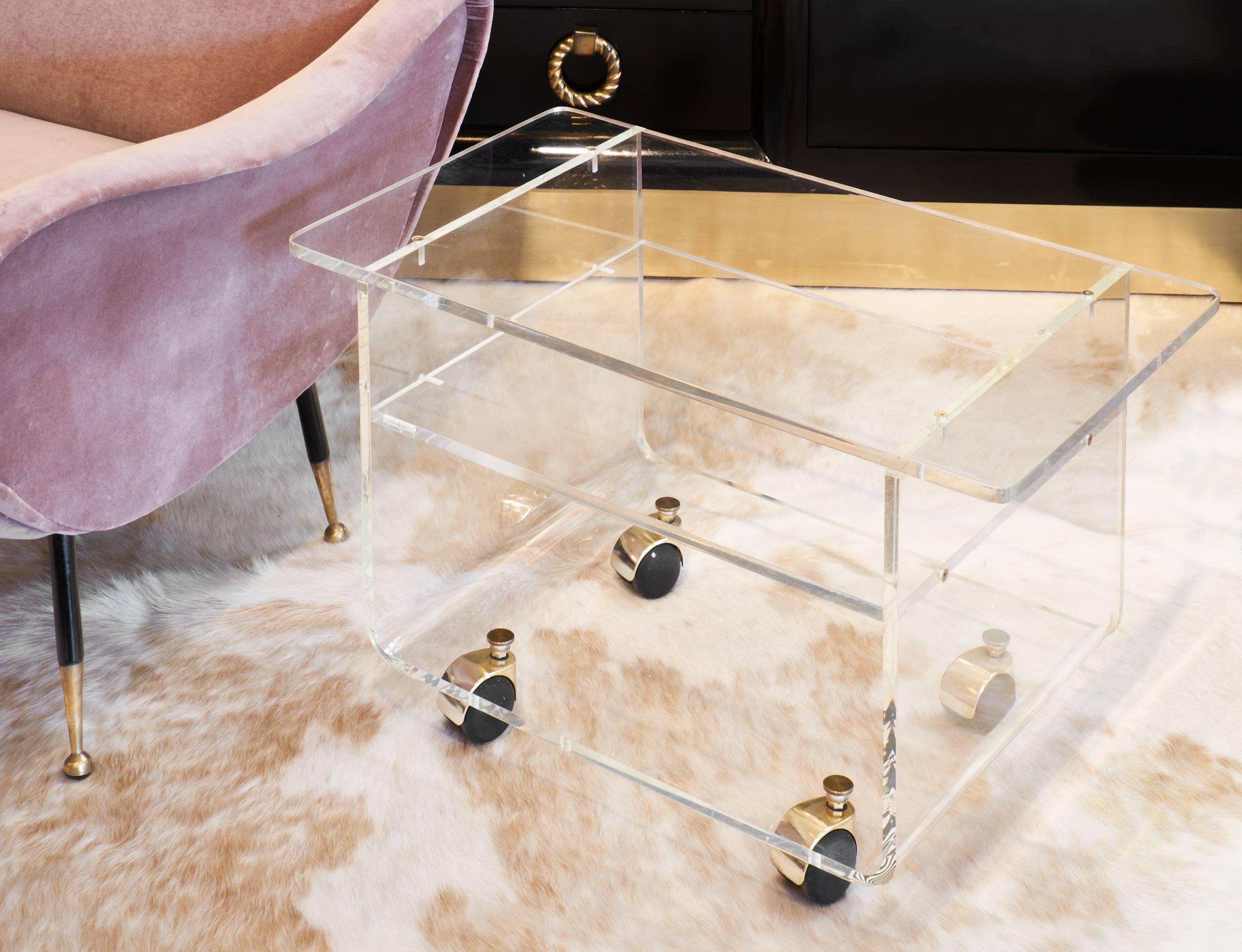 French vintage bar cart or occasional table on wheels, formed of Lucite (clear acrylic) with brass fasteners. A unique shape with a long top, curving base and a middle shelf.