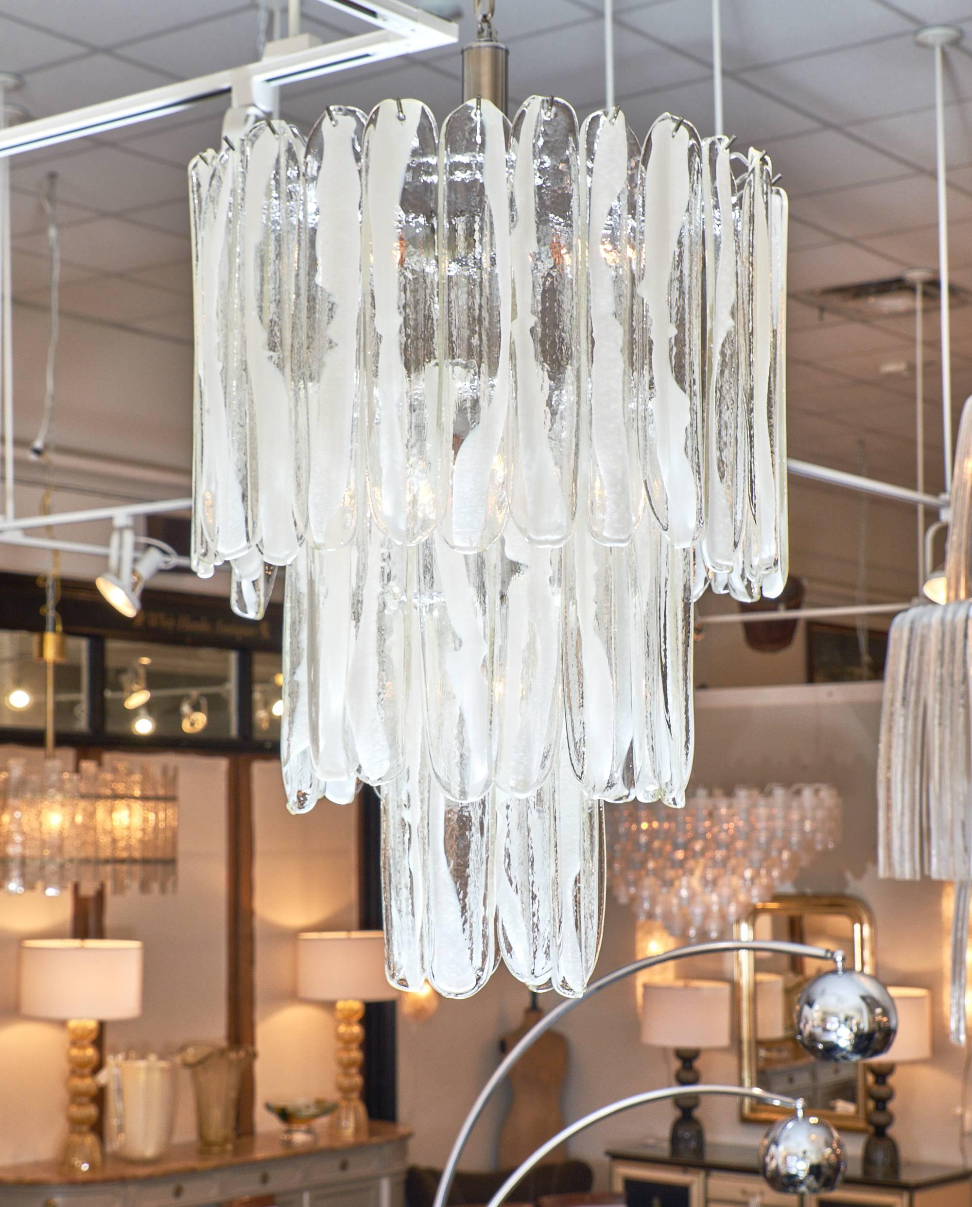Beautiful pieces of Murano glass in a rippled shape hang to create this stunning tiered chandelier. In the Incamicciato technique each piece is a clear transparent color with ribbons of white opaline. The fixture has three tiers, each with a smaller