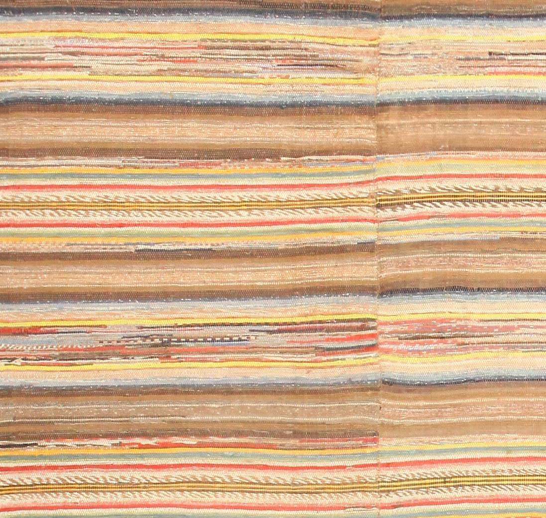 This antique American rag rug classically combines an eclectic mix of colors with a traditional tartan pattern to create a warm and engaging design that is quite reminiscent of mid-century modern rugs. There are distinct points of variation that