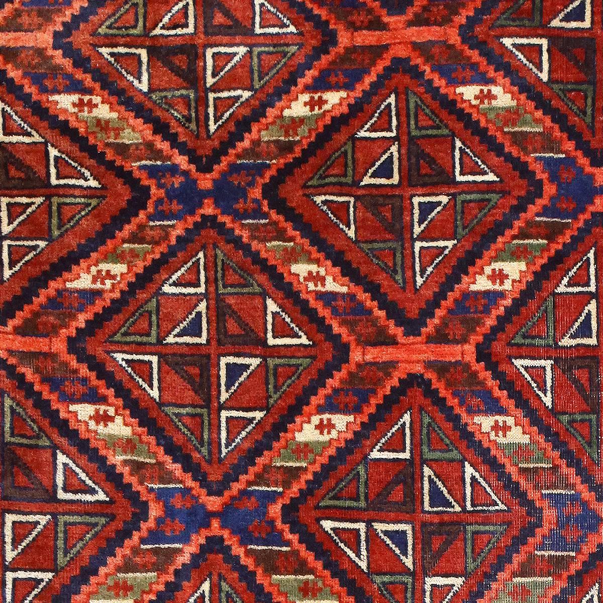 A pattern of diamonds with stair-step edges repeats across the body of this antique Afghan rug, starkly vibrant in red, orange and blue, accented with white, light green and pale yellow. The riot of colors is perfectly organized into a striped