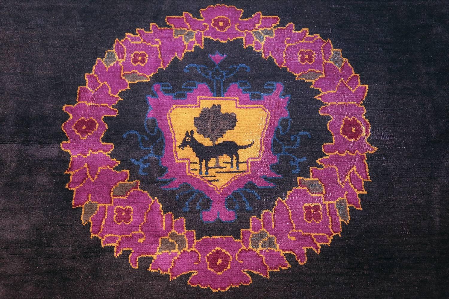 Art Deco Chinese rug, early 20th century. This elegant Chinese rug carries a single purple, red, green, blue and golden medallion in a black field. It depicts the bountiful gift of abundant life through a green and red wreath encompassing a gold