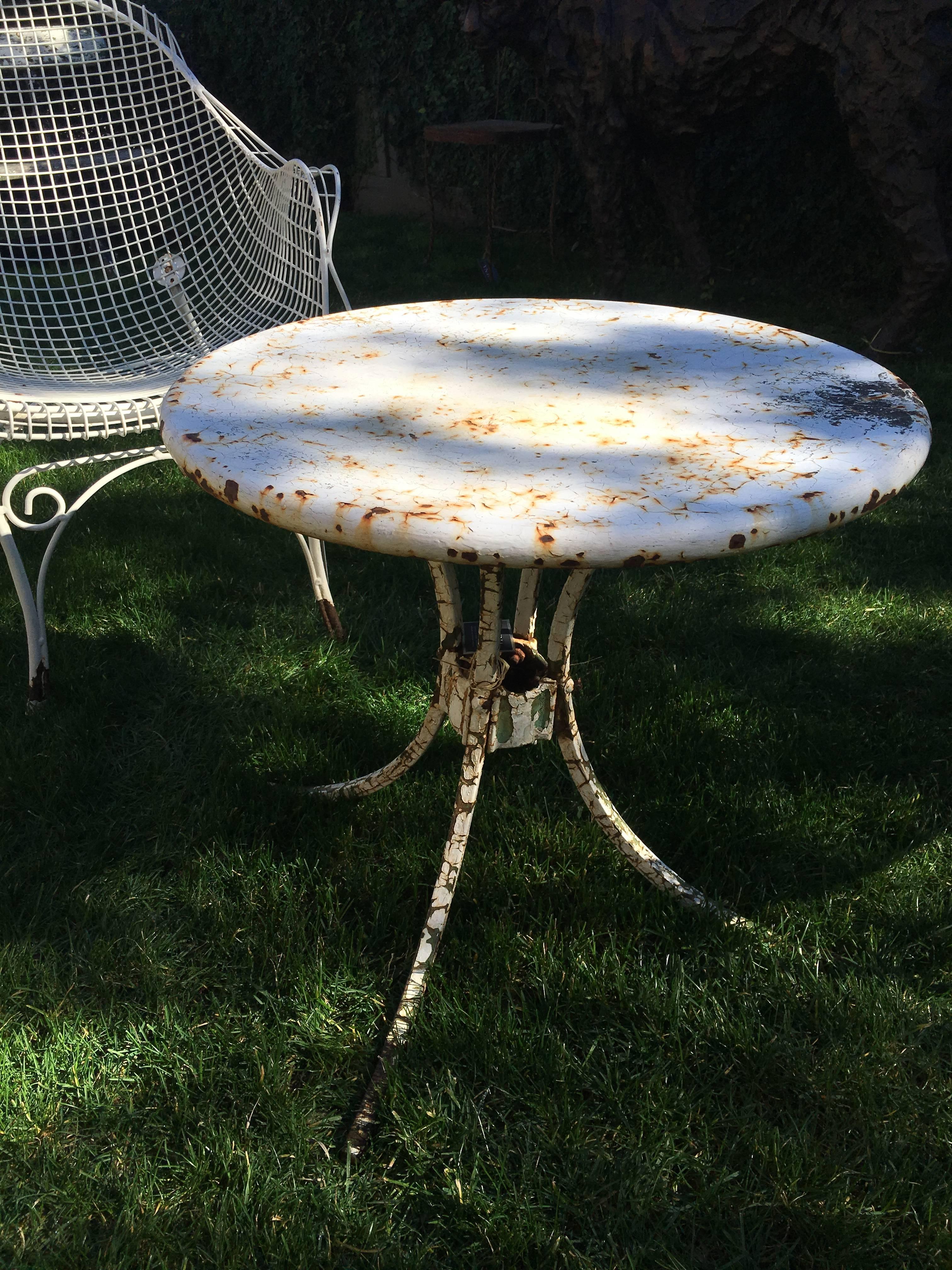 Table d'appoint de jardin en métal américain vintage, circa 1950. Surface de la table peinte en blanc avec d'épaisses craquelures. Les jambes sont peintes en blanc également, avec une couche de vert révélée en dessous. Plateau et pieds en deux