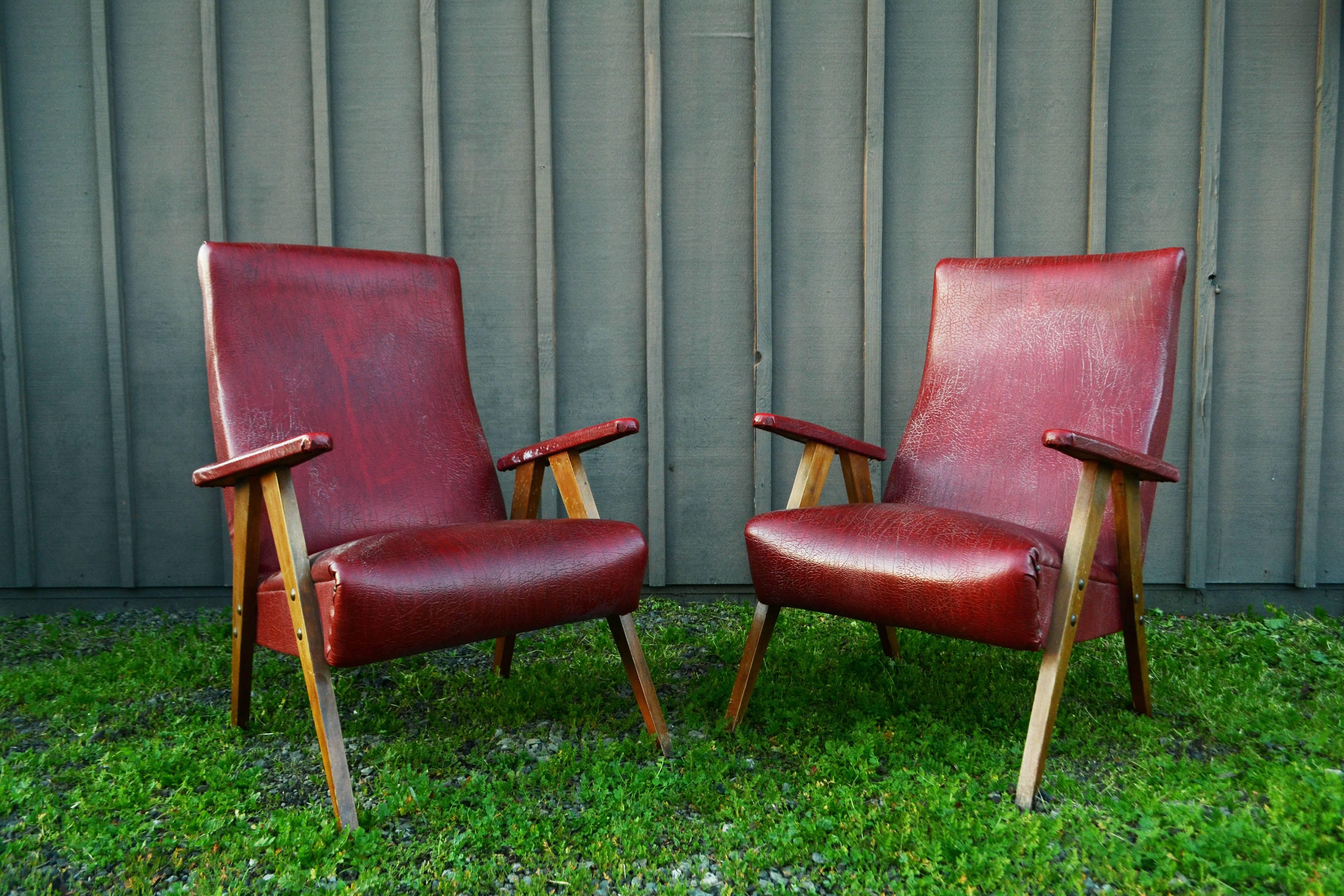 Pair of vintage red leather armchairs with wooden legs and upholstered arms.
