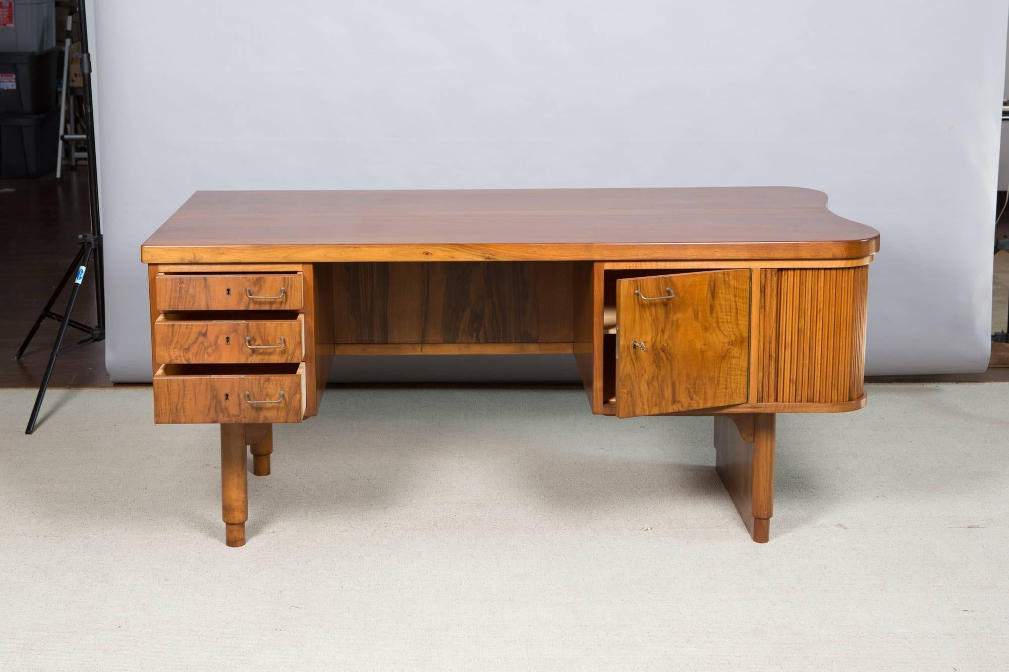 Beautiful midcentury Danish desk with locking drawers, sliding tambour side doors and unique storage shelf on the front side of the desk that is great for books and display items. Great original condition. Includes key.