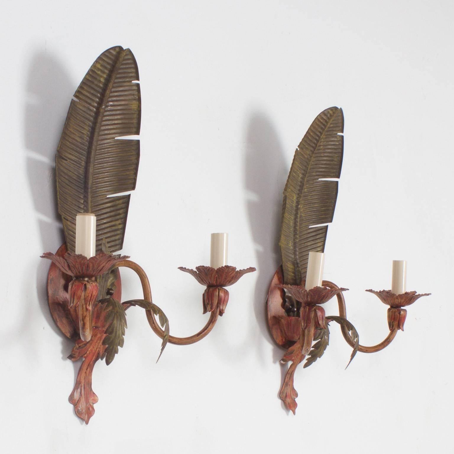 Whimsical pair of Mid-Century tole palm leaf sconces with a delightful tropical flavor and painted with muted hues. Designed with a classical two light form and acanthus details.

.