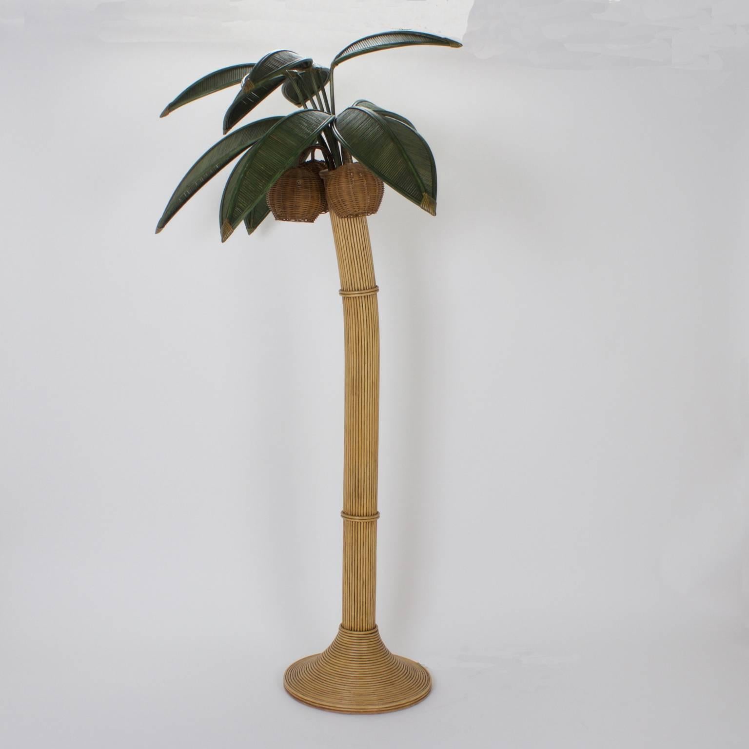 Whimsical, stylized palm tree floor lamp crafted with reed in a well thought out sophisticated design. Having subtle green painted palm leaves and three wicker coconuts that are lights, simple ringed trunk, and Art Deco style base. 

