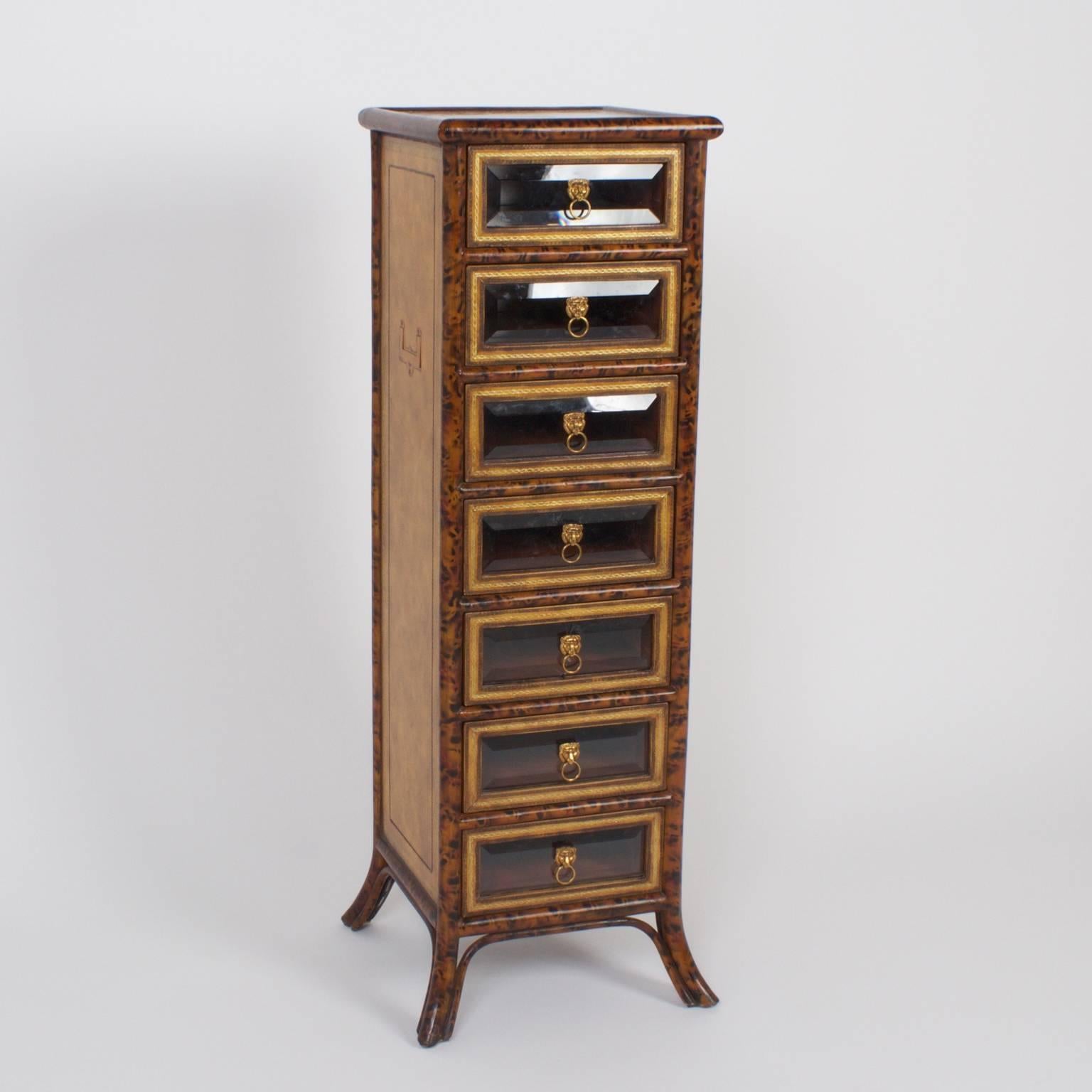 Tall, stately seven-drawer chest with a faux bamboo frame painted with a tortoiseshell technique, and paneled sides with tooled leather and inset campaign style hardware. The drawers have tooled leather borders with beveled glass and lion head brass