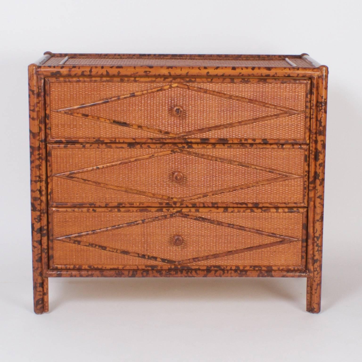 Mid century three drawer chest or nightstand with down to earth organic textures. The frames have a faux tortoise over bamboo finish. The case is covered in grasscloth and decorated with geometric patterns.