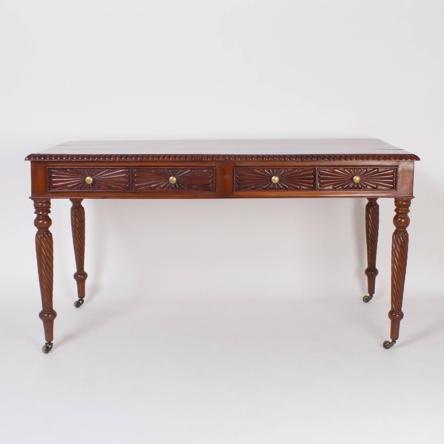 Antique, British Colonial writing desk or library table from India, crafted with well grained mahogany in a handmade pegged construction. Featuring a beaded cornice, two carved drawer fronts, and turned legs on casters. Cleaned, waxed, and ready for