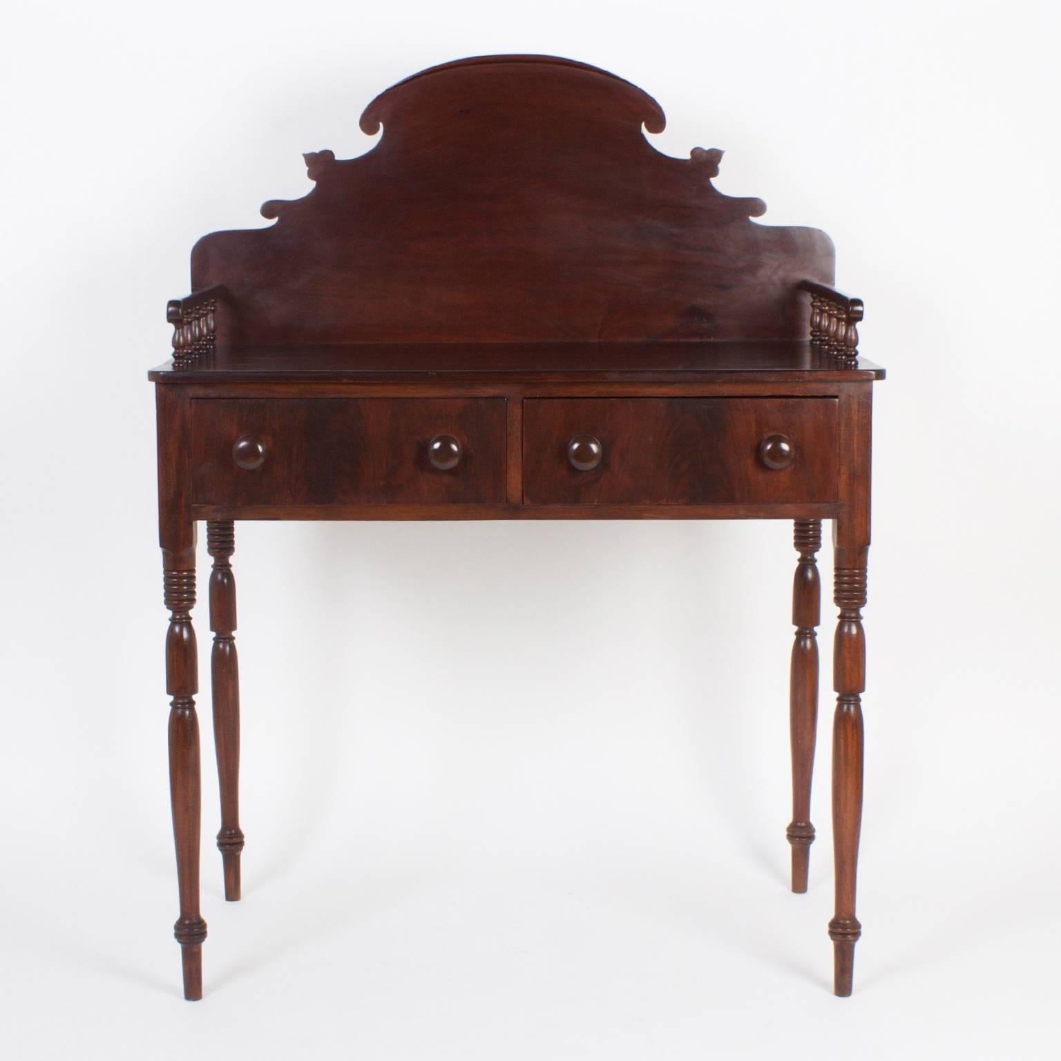 Handsome, antique British colonial server or bar probably from St. Croix in the West Indies. Crafted with mahogany and featuring a dramatic back splash, side galleries with turned supports, two drawers and long elegant turned legs. The form and