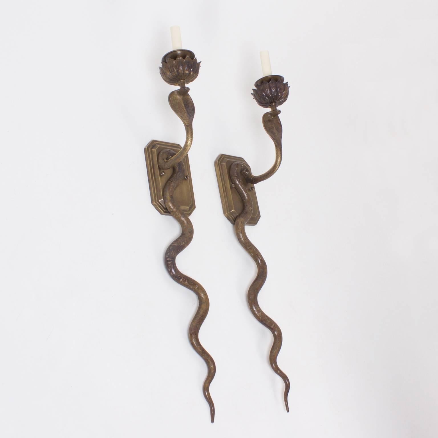Charming pair of cast bronze cobra wall sconces with flower shaped candle cups and floral engravings throughout. These snakes have a perfect patina and carry the allure of exotic locations. Newly wired. 

 