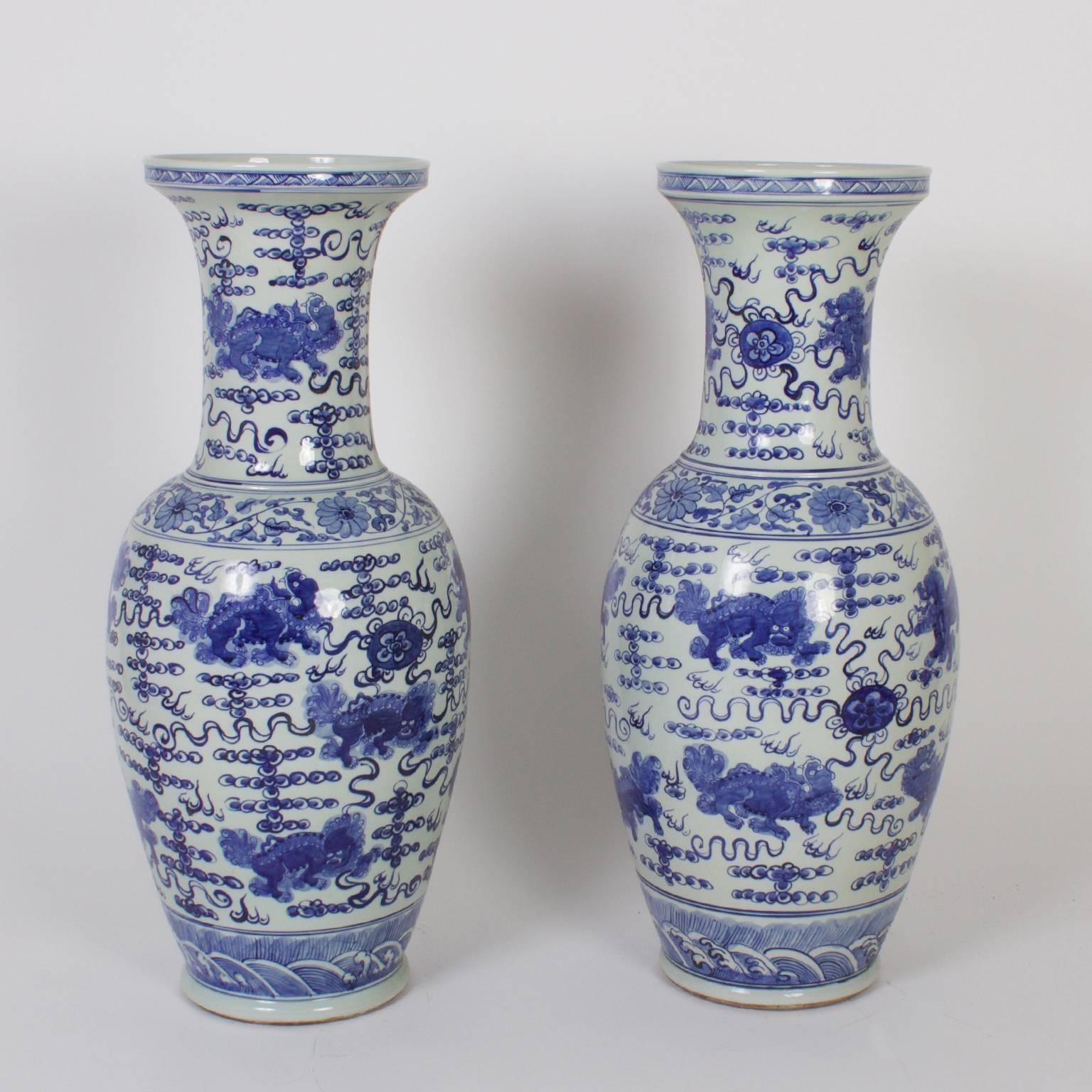 Impressive pair of Chinese blue and white porcelain palace vases with dragons and lions set against squiggly lines and floral bands with ocean waves at the base.
  