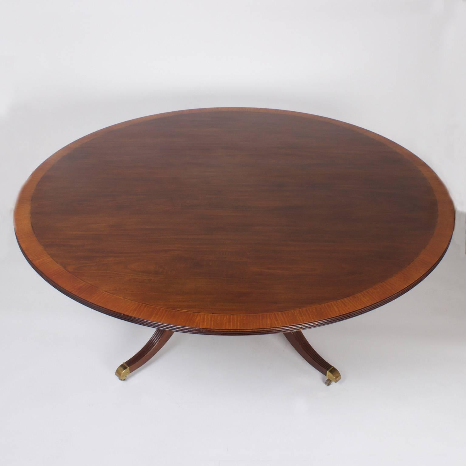 Handsome Mahogany round dining table with a cross banded inlaid top and a beaded edge. The pedestal base has a four column box on a plateau supported by four Duncan Fyfe style legs on brass feet and casters. Signed “Baker Collectors Edition” on the
