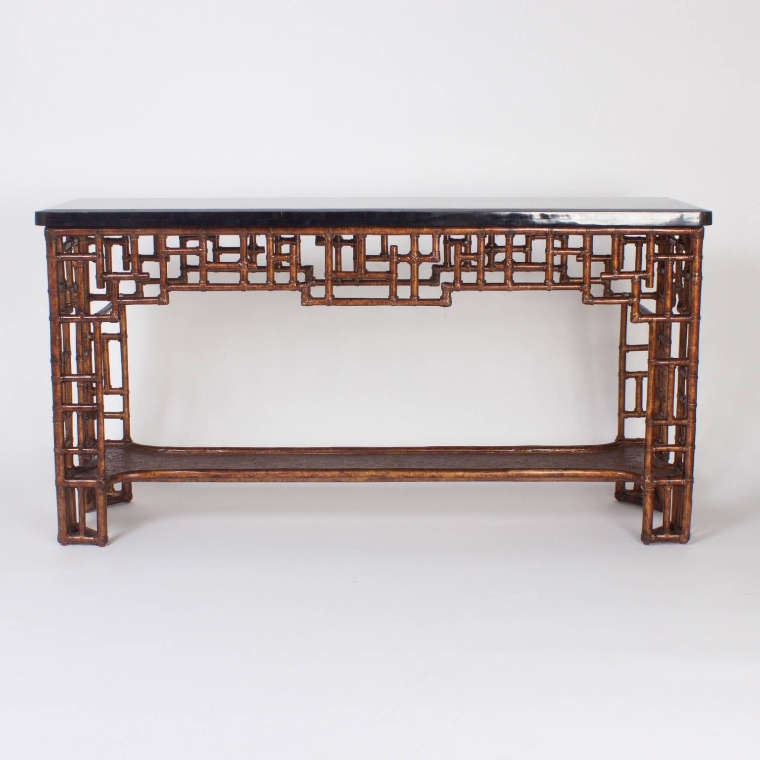 Maitland-Smith Mid-Century Chinese Chippendale console featuring a lacquered penshell top with an inlaid geometric design. The faux bamboo base is crafted with metal and supports a sculptural lower tier. Superior quality and design make this piece a
