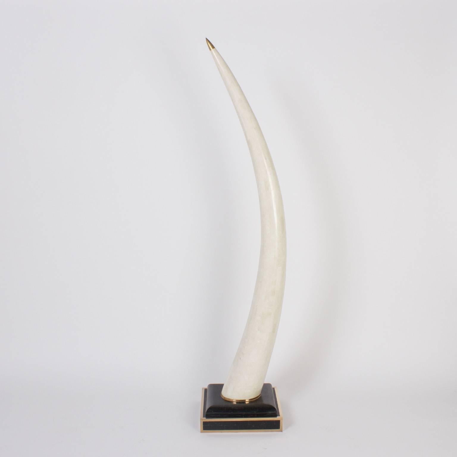 Chic, mid century pair of faux elephant tusks crafted with stone and capped with brass points, presented on tessellated black stone bases bordered with brass. Will add a dramatic element to any interior.
