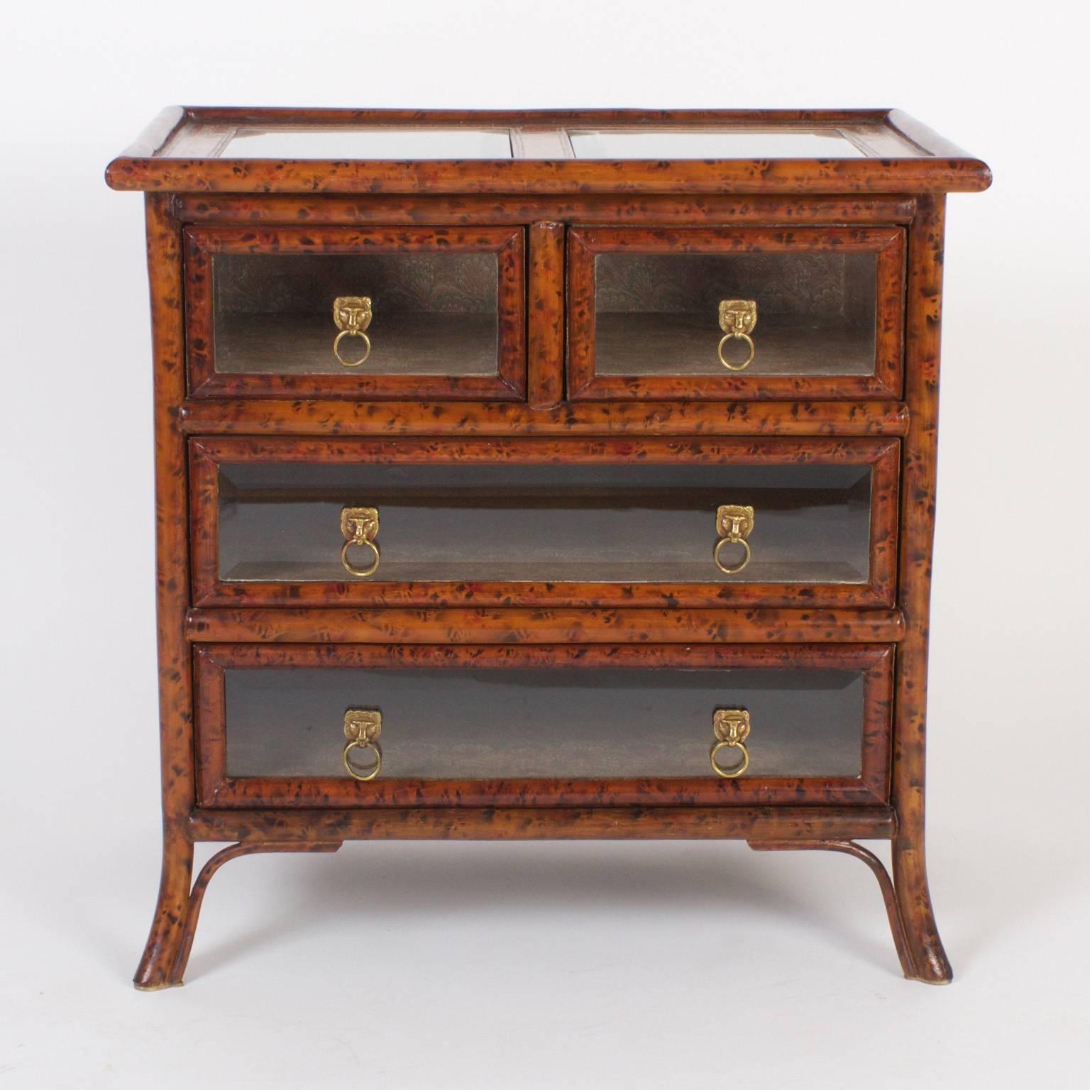 Mid century Maitland-Smith chest of drawers or display chest featuring a beveled glass top and drawer fronts, faux bamboo frame and tooled leather sides and borders. The insides of the drawers are covered with Classic book lining paper and the