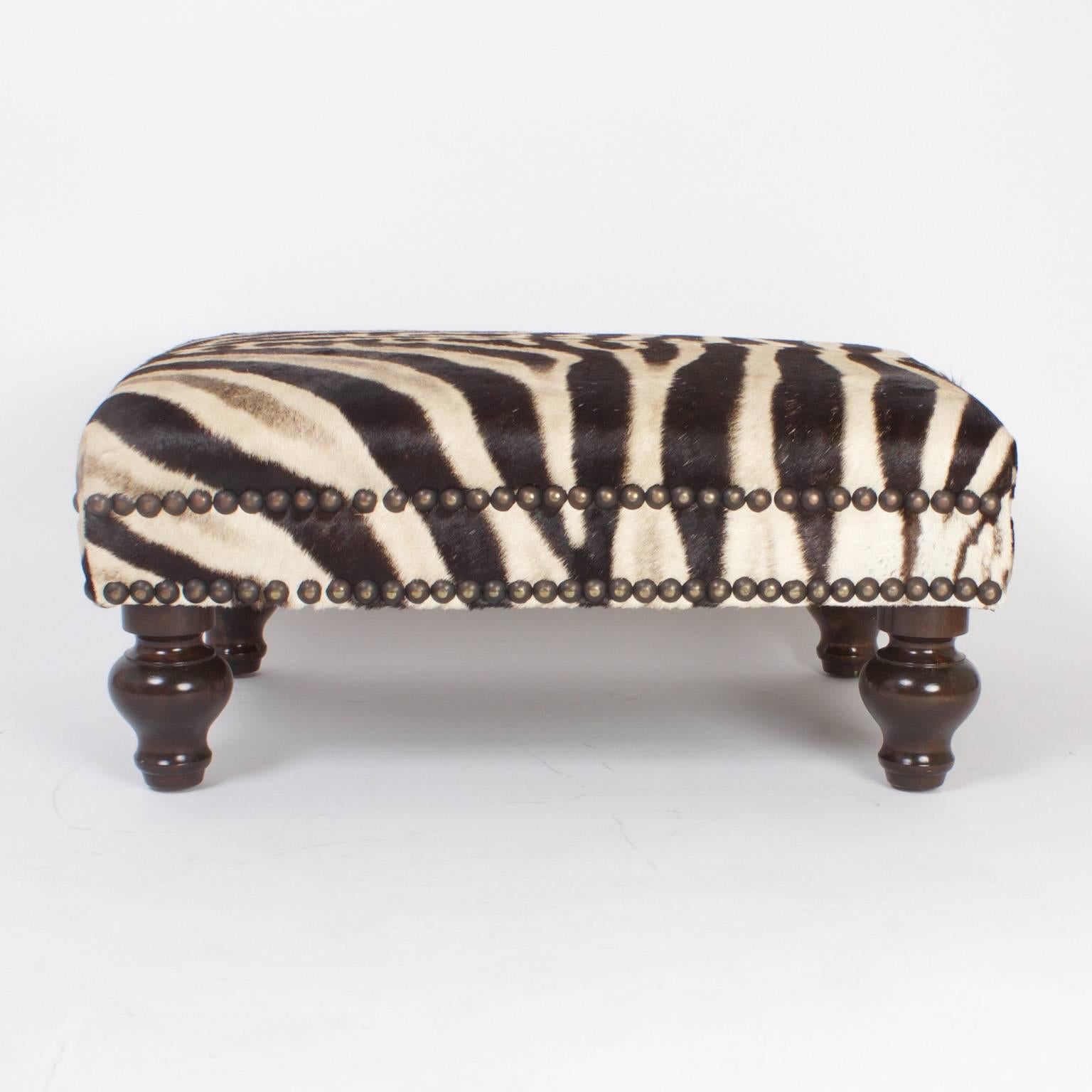 Handsome rectangular bench or ottoman upholstered in natural organic zebra hyde, decorated with brass studs and supported by Classic turned wood feet.