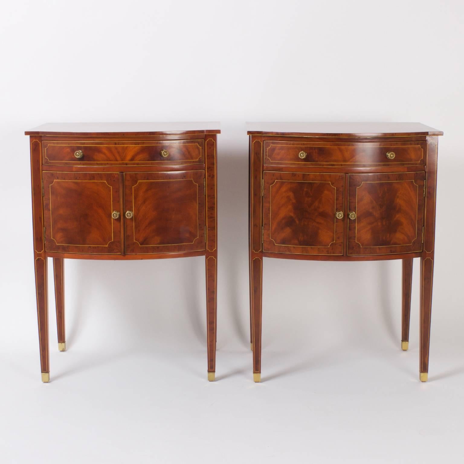 Elegant pair of bow front mahogany nightstands or cabinets featuring exotic flame mahogany veneers and satinwood string inlays that highlight the Classic form. Signed Maitland-Smith on a brass plaque.
                