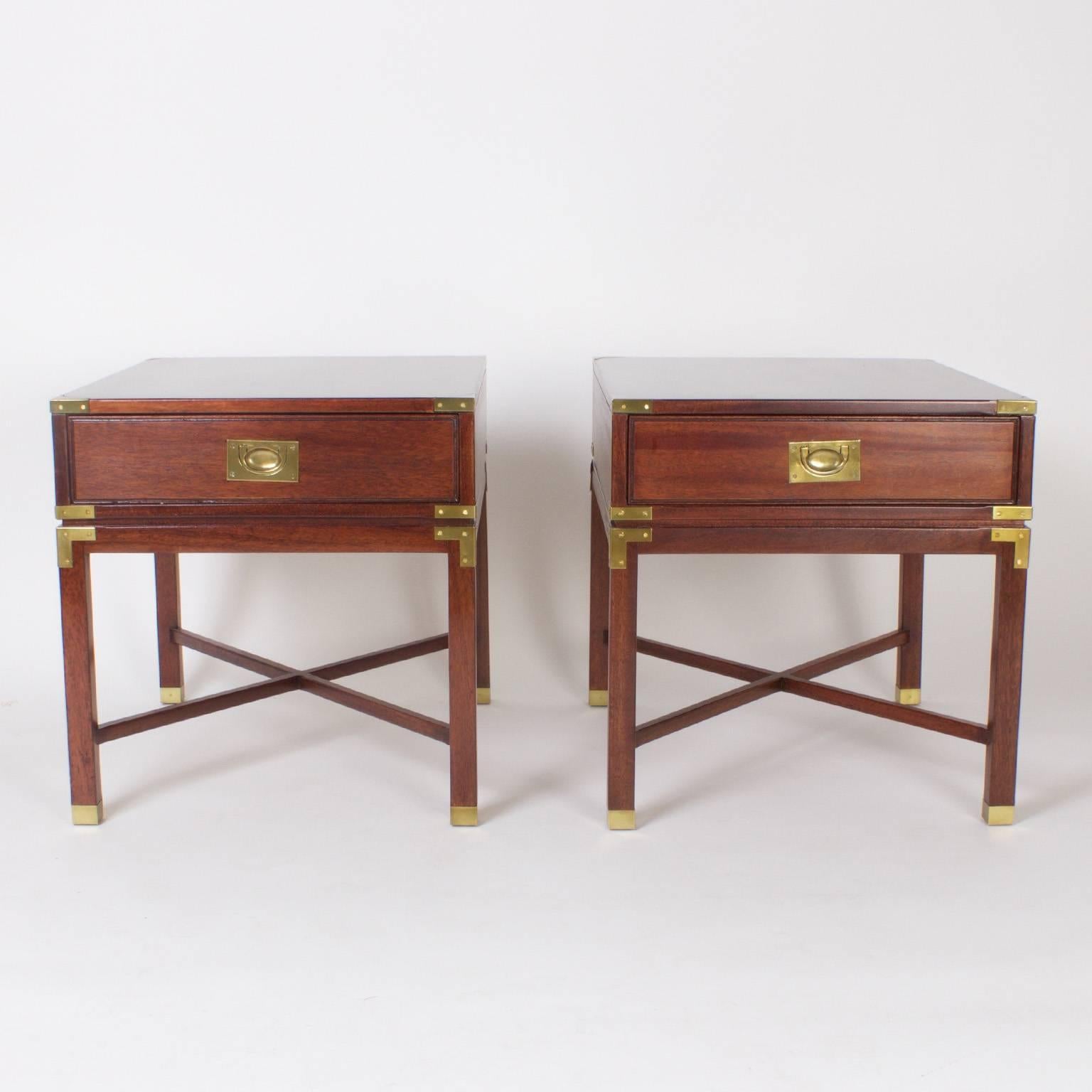 Dapper pair of Mid-Century, mahogany Campaign stylized nightstands or end tables. Featuring brass hardware, elegant cross stretchers and brass capped feet. Signed Heritage in a drawer. 
  