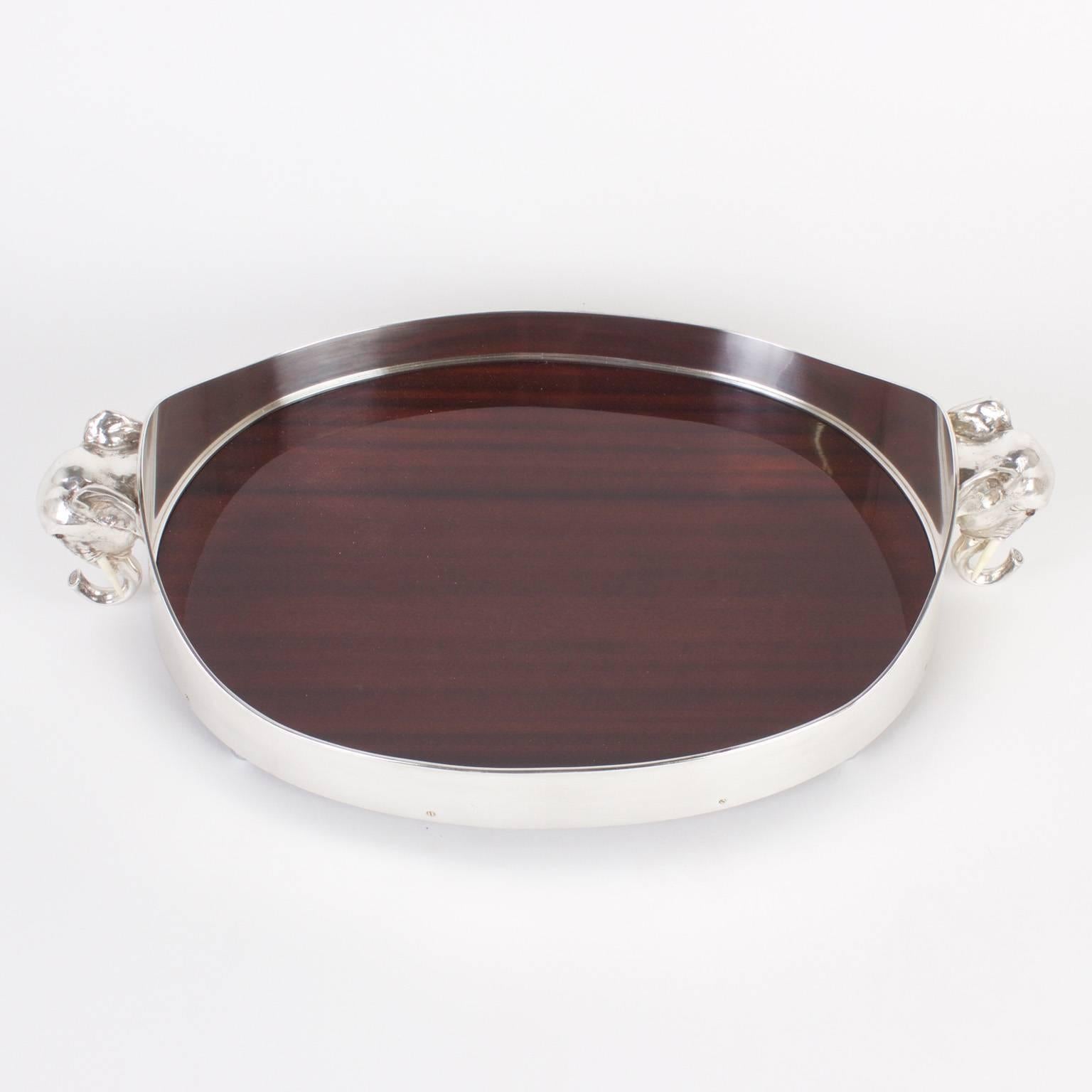 Elegant serving tray with a silvered metal frame and elephant head handles. The plateau is mahogany, making a sharpe statement against the silver frame. The whole tray sits on Classic ball feet. A pair is also available. Please inquire for more