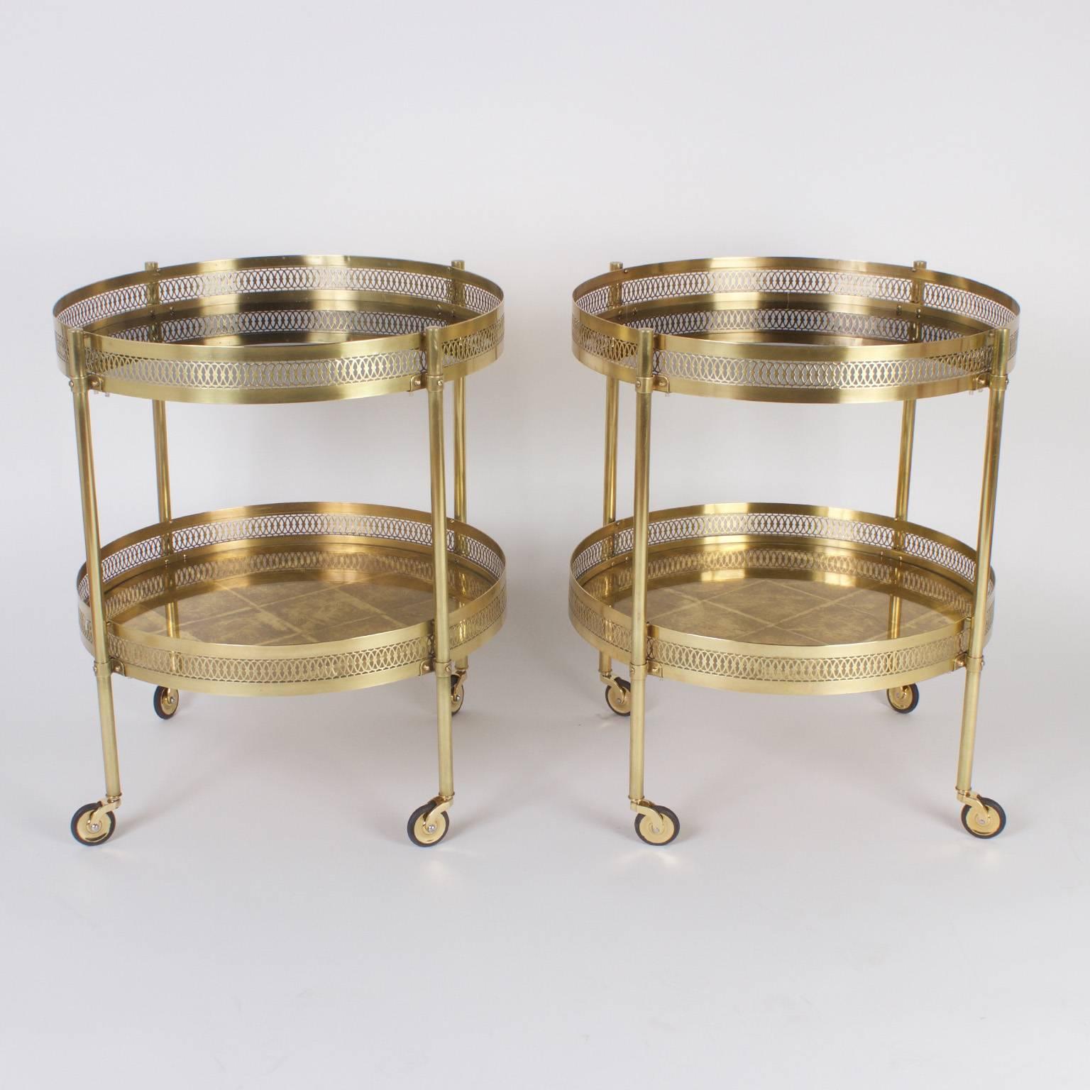 Chic pair of round brass serving carts, tables or trolleys that have a timeless international flair. The two tiered gallery design gives service and storage. The top tier is reverse painted black glass, the bottom is reverse painted gold leaf glass.