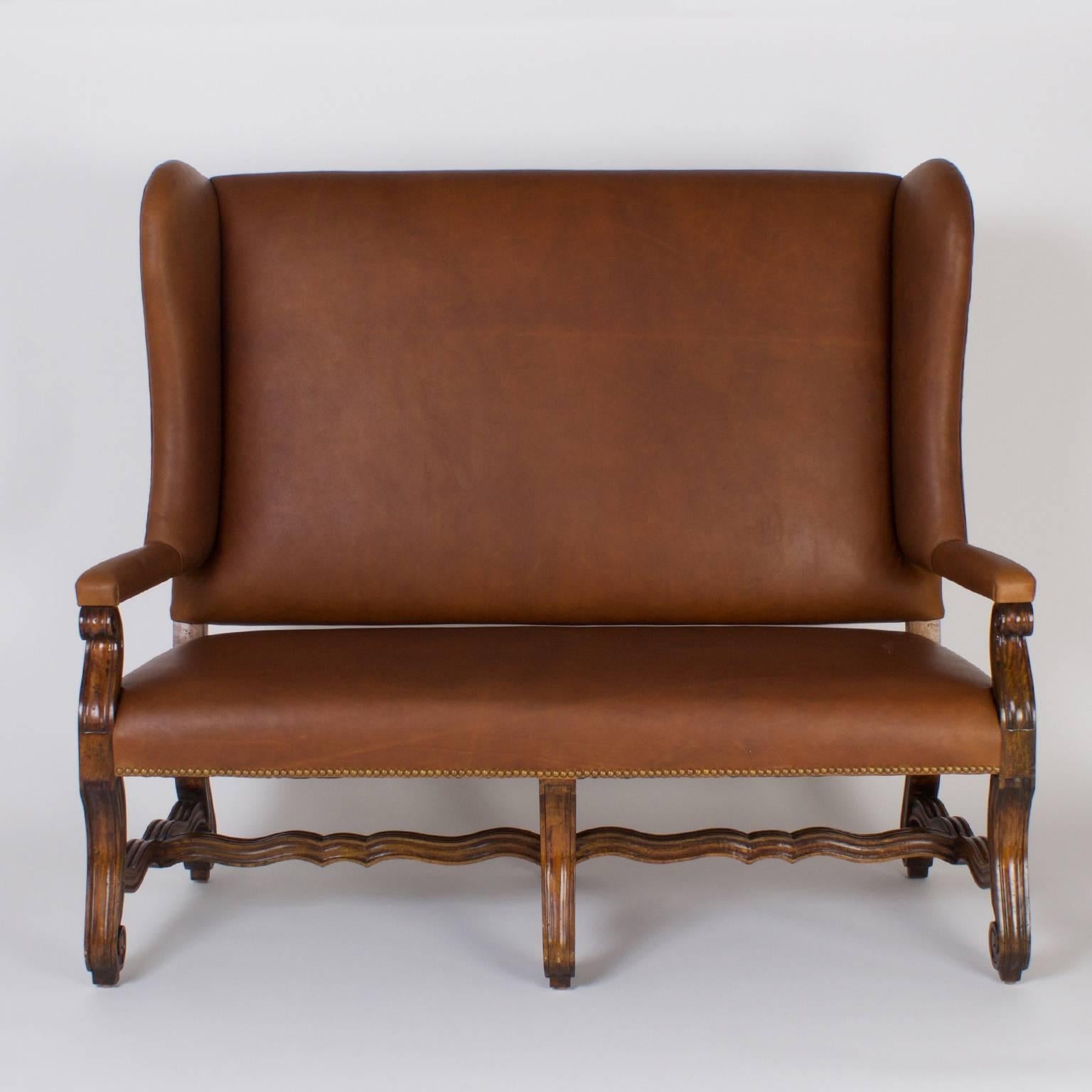 Stately Ralph Lauren brown leather bench, settee or couch with a bold upright stance, reminiscent of an antique Spanish or French court design. Featuring a winged back, padded arms and dramatic scrolled legs joined by scalloped stretchers.
    