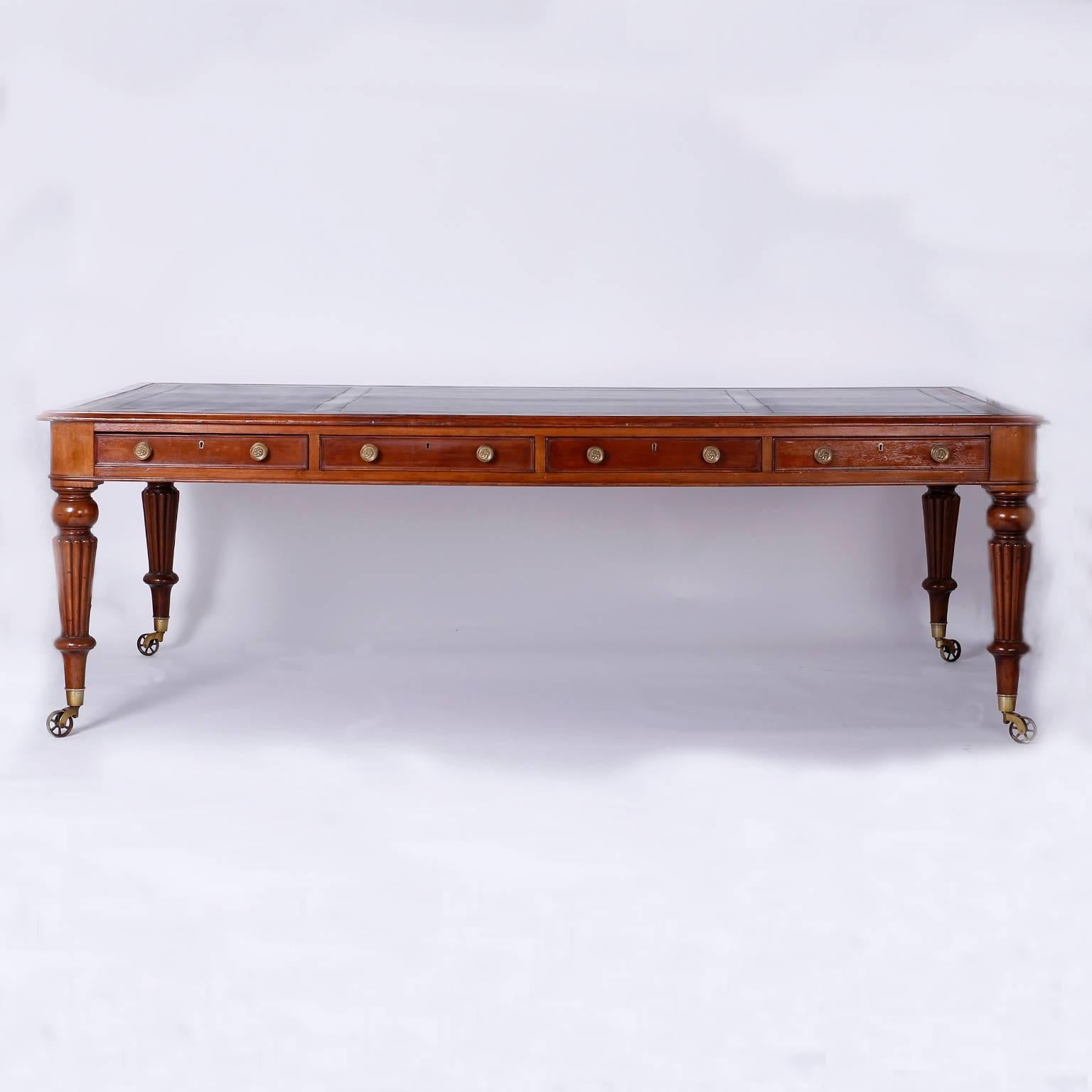 Stately, antique English mahogany partners desk or library table having a lush dark brown leather top with a gold leaf greek key border. The case has four drawers with brass hardware on either identical side. The legs are lathe turned and have