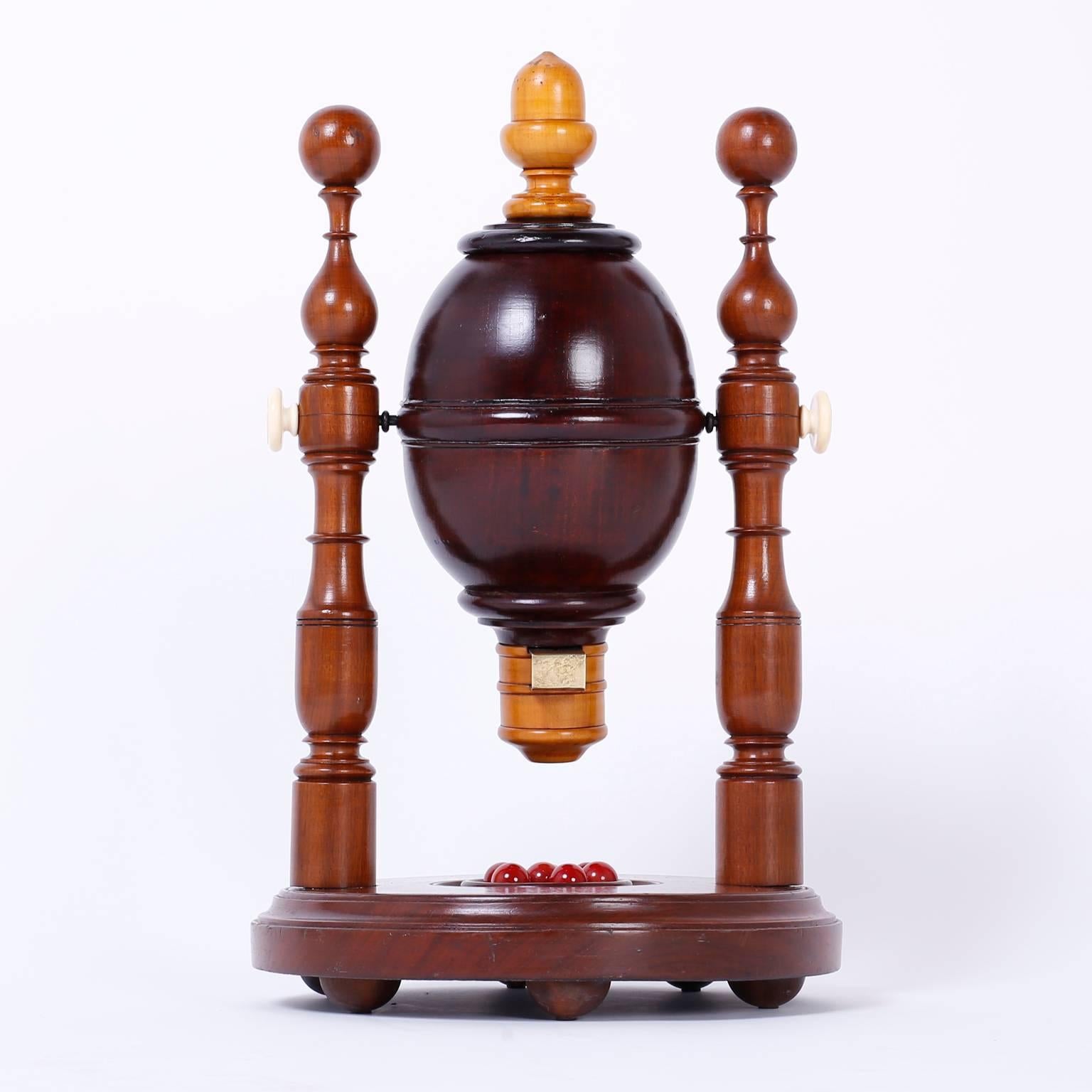 Curious mechanical lottery apperatice that has a hardwood spinning canister with pine cap and spout, supported by two turned mahogany posts on a round wood base with ball feet. The perfect combination of art and function.