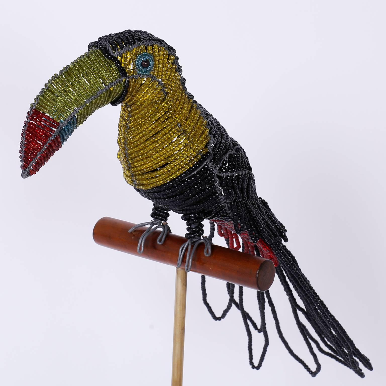 Amused and amusing bird sculpture crafted with glass beads on a metal frame and sitting on a wood perch supported by a brass rod on a Lucite base.
