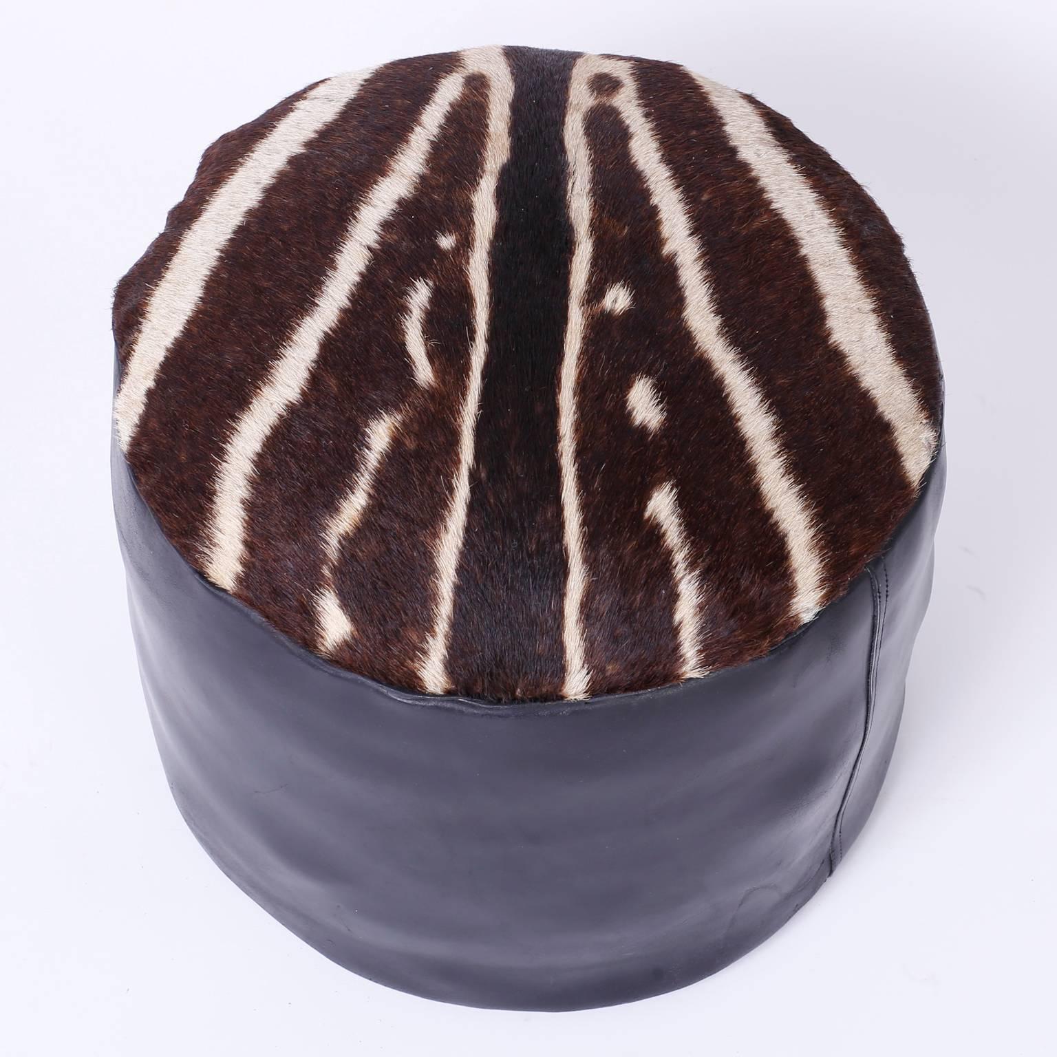 In vogue, round foot stool or hassock with black leather sides and a well placed zebra hide top. Simple form, iconic design.