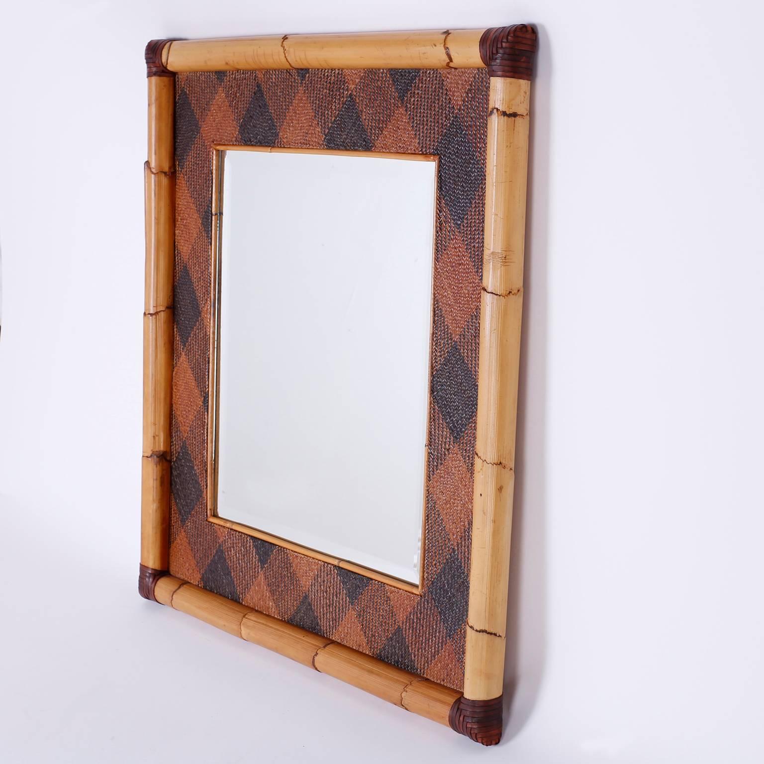 Handsome mirror in a frame crafted with bamboo and wrapped at the corners in an unusual argyle wicker pattern. The mirror is beveled. Stamped on the back Mackenzie Childs 1983.