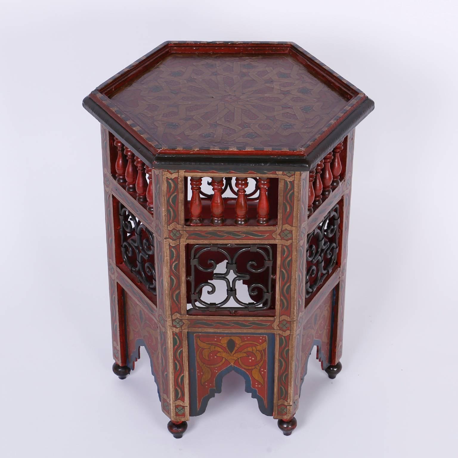 Exotic Moroccan drink stand or occasional table with a hexagon form and open air panels decorated with spindles and wrought iron. Featuring delightful geometric and floral paintings throughout and Moorish arches over onion bulb feet.
