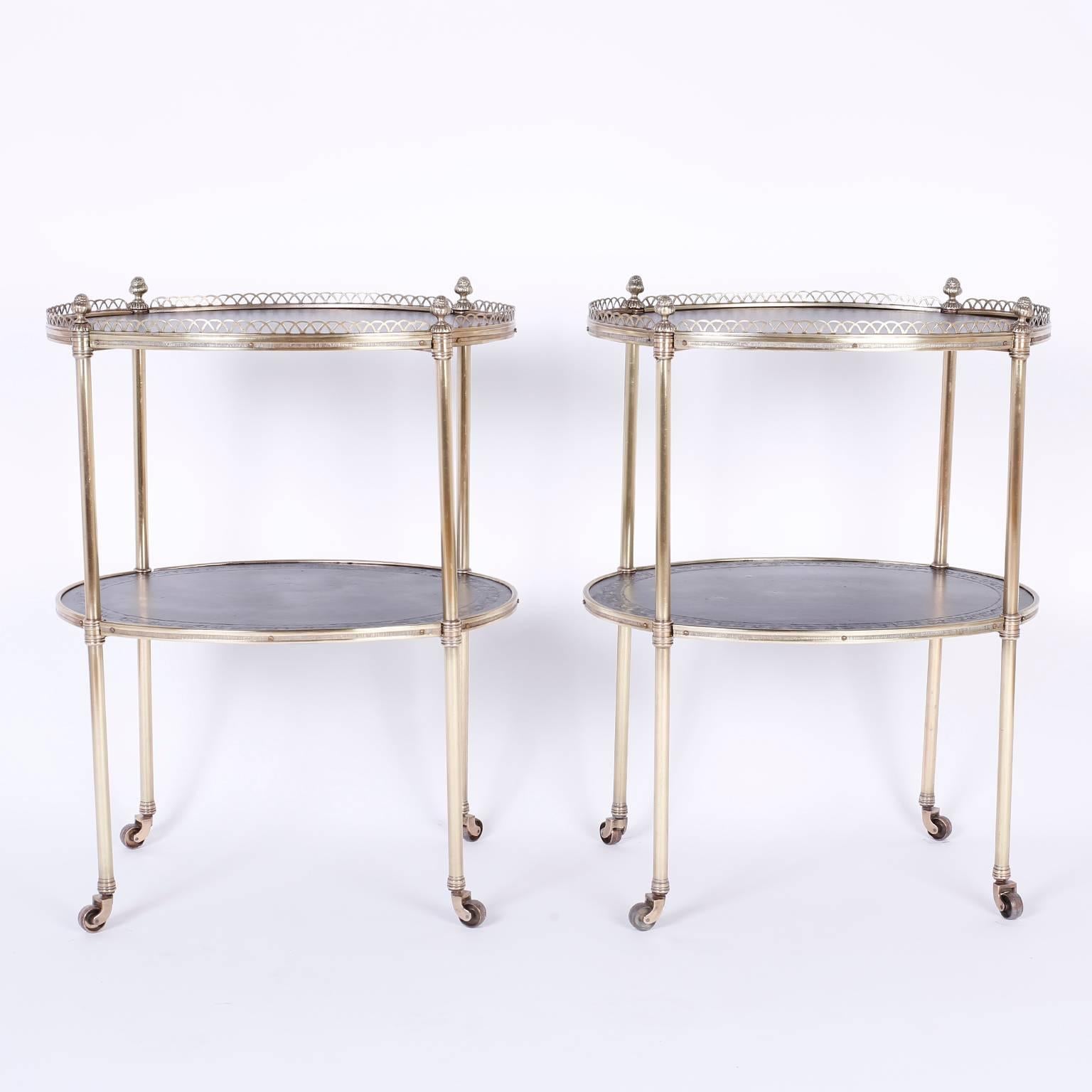 Chic pair of midcentury brass and black leather serving carts that can function as end tables or bedside stands. The top tier features a brass gallery punctuated by four acorn finials. Both plateaus have tooled leather eagles and plumbs around the