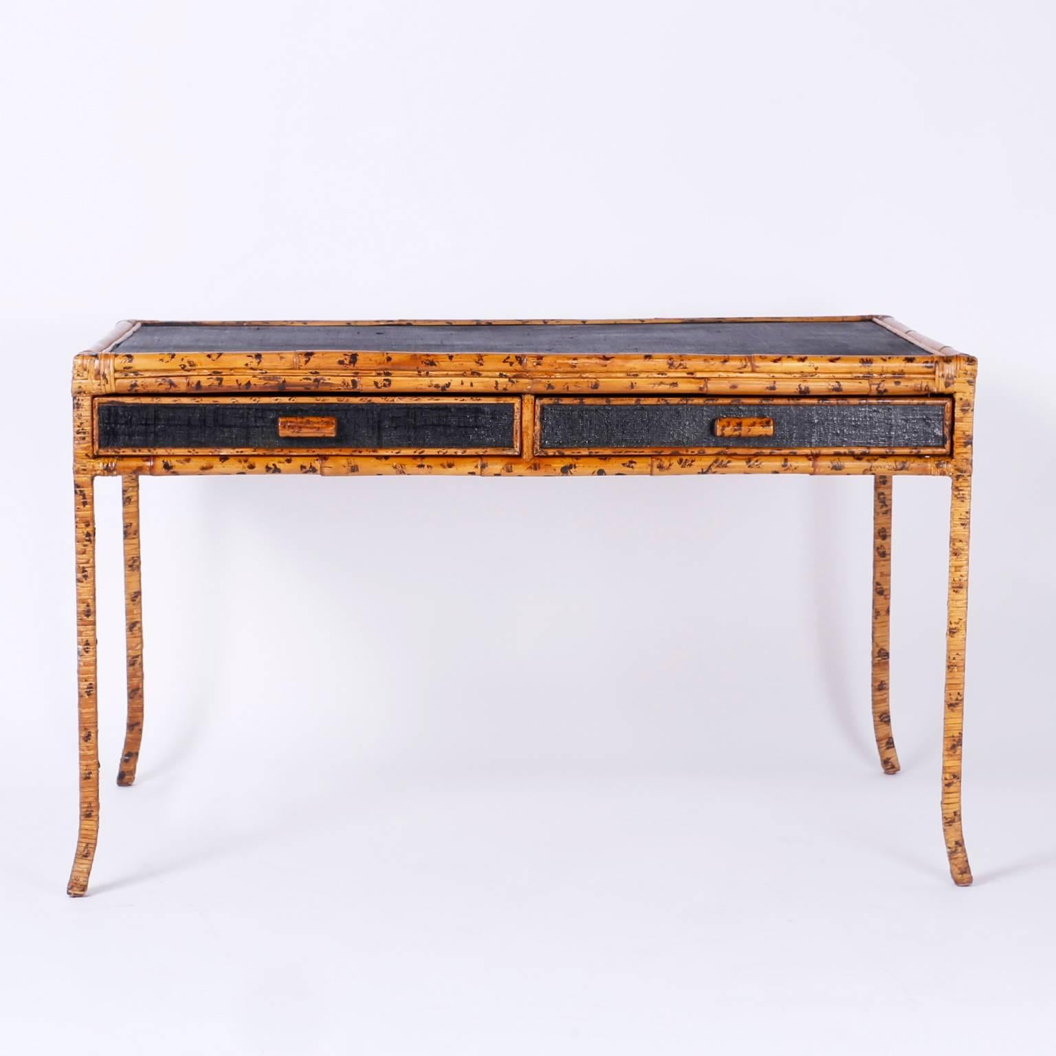 Chic midcentury interpretation of British colonial style desk or writing table with a faux bamboo frame and black painted grasscloth panels on the case. The elegant splayed legs are metal wrapped with decorated wicker. With an alluring organic
