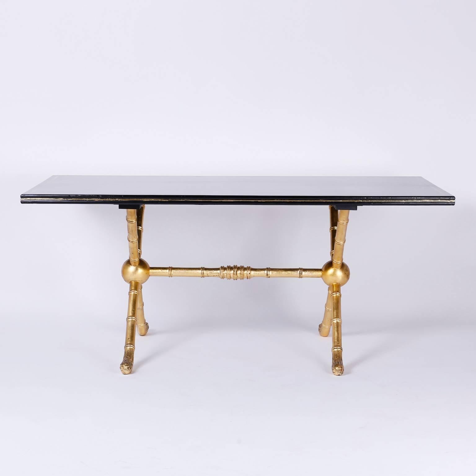Unusual table with a black lacquered gilt trimmed top. The well detailed carved wood bamboo X-shaped legs are connected by a turned stretcher that is all in gold leaf. This can be utilized as a dining, writing or display table.