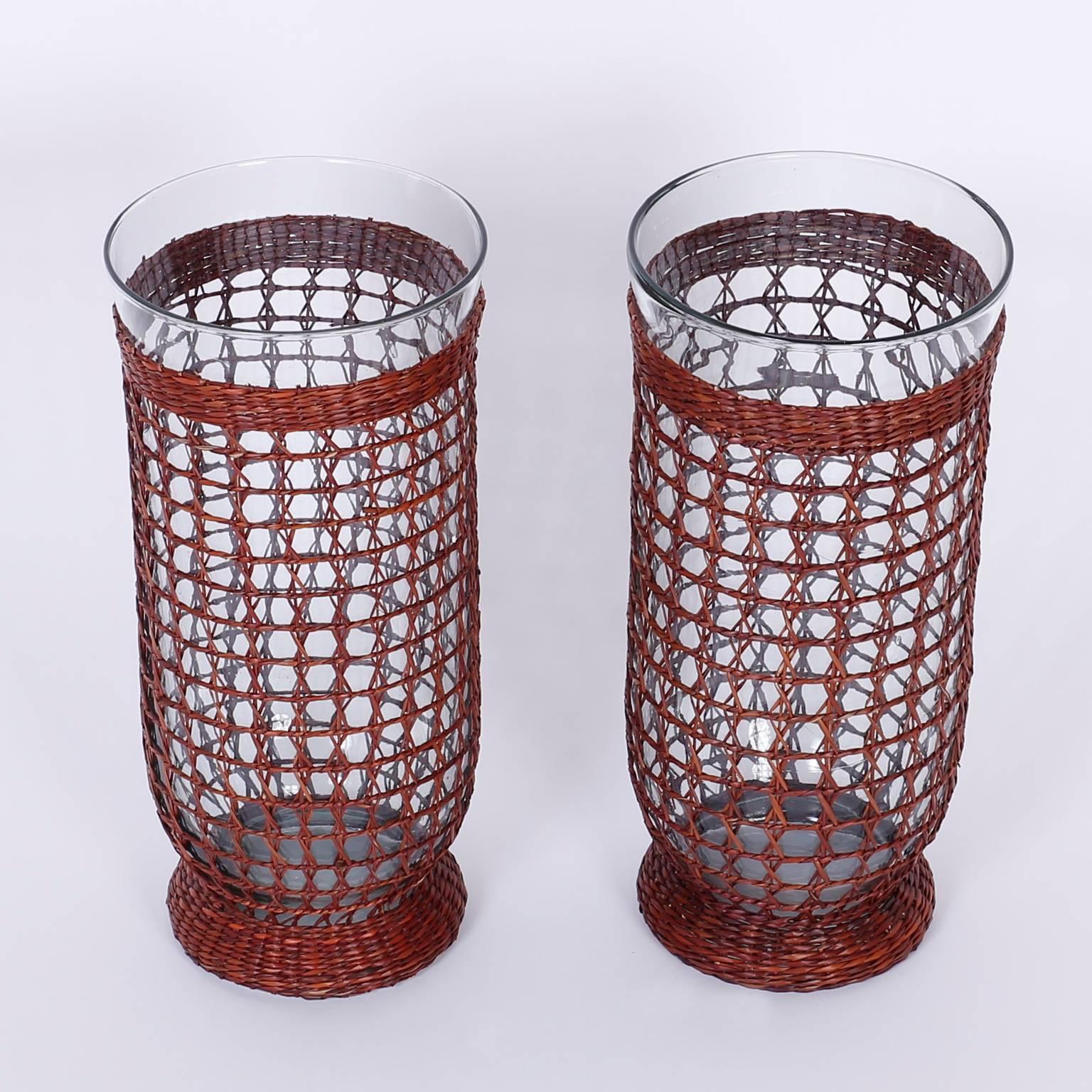 Chic pair of hurricane candleholders composed of Classic form handblown glass wrapped in fish net wicker or cane. Casual sophistication at its best.
 