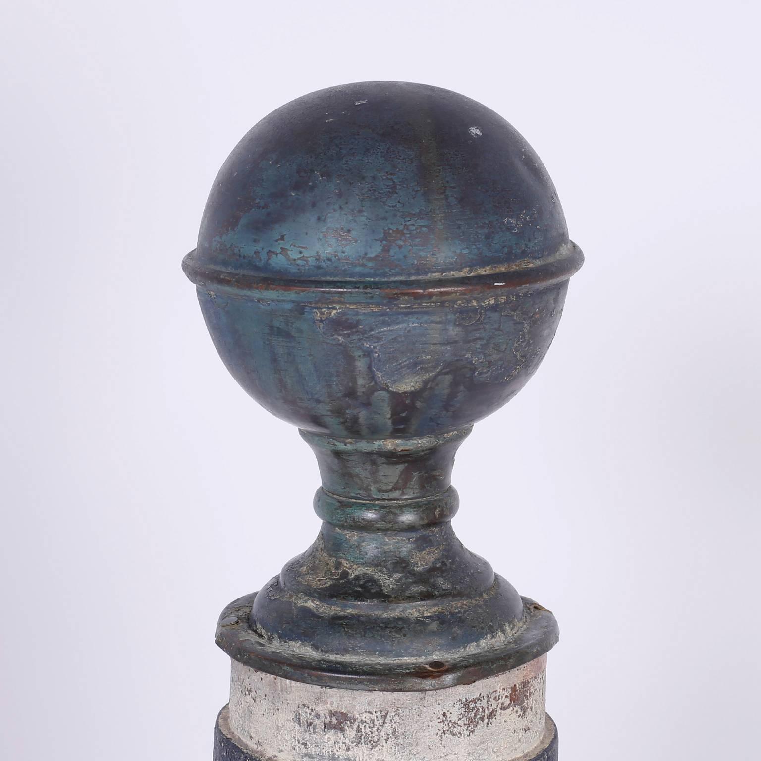 Folky barber's pole with Classic architectural form, topped with a brass ball on stand that has acquired an alluring patina. The shaft is a tapered cylinder on a rectangular plinth. This rare object has retained its original red white and blue, now