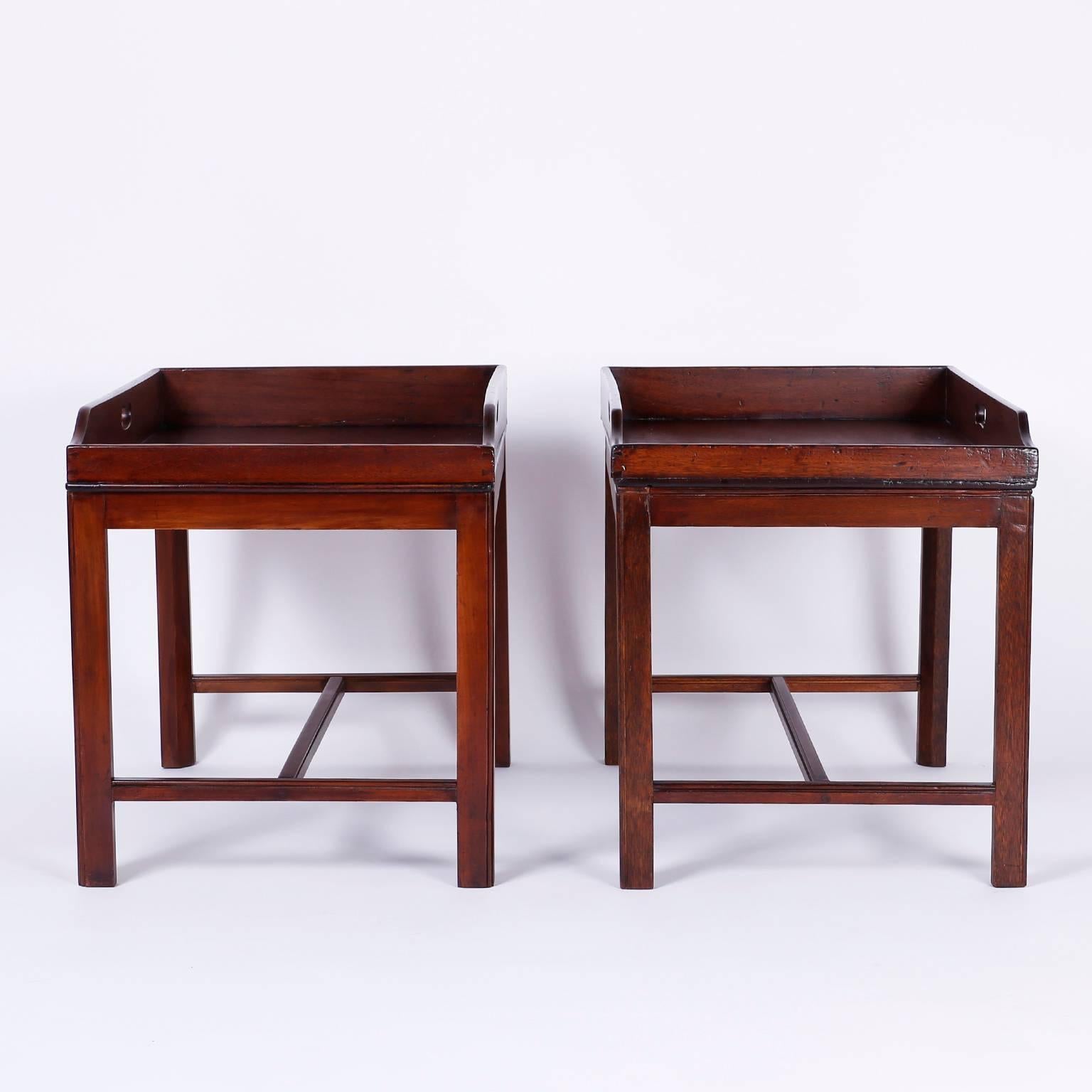 Handsome pair of stylized butlers tray tables that can function as end tables, nightstands or for serving. The attached tops have galleries with cut-out handles and sloped fronts. The bases have an unadorned Georgian form giving these tables a